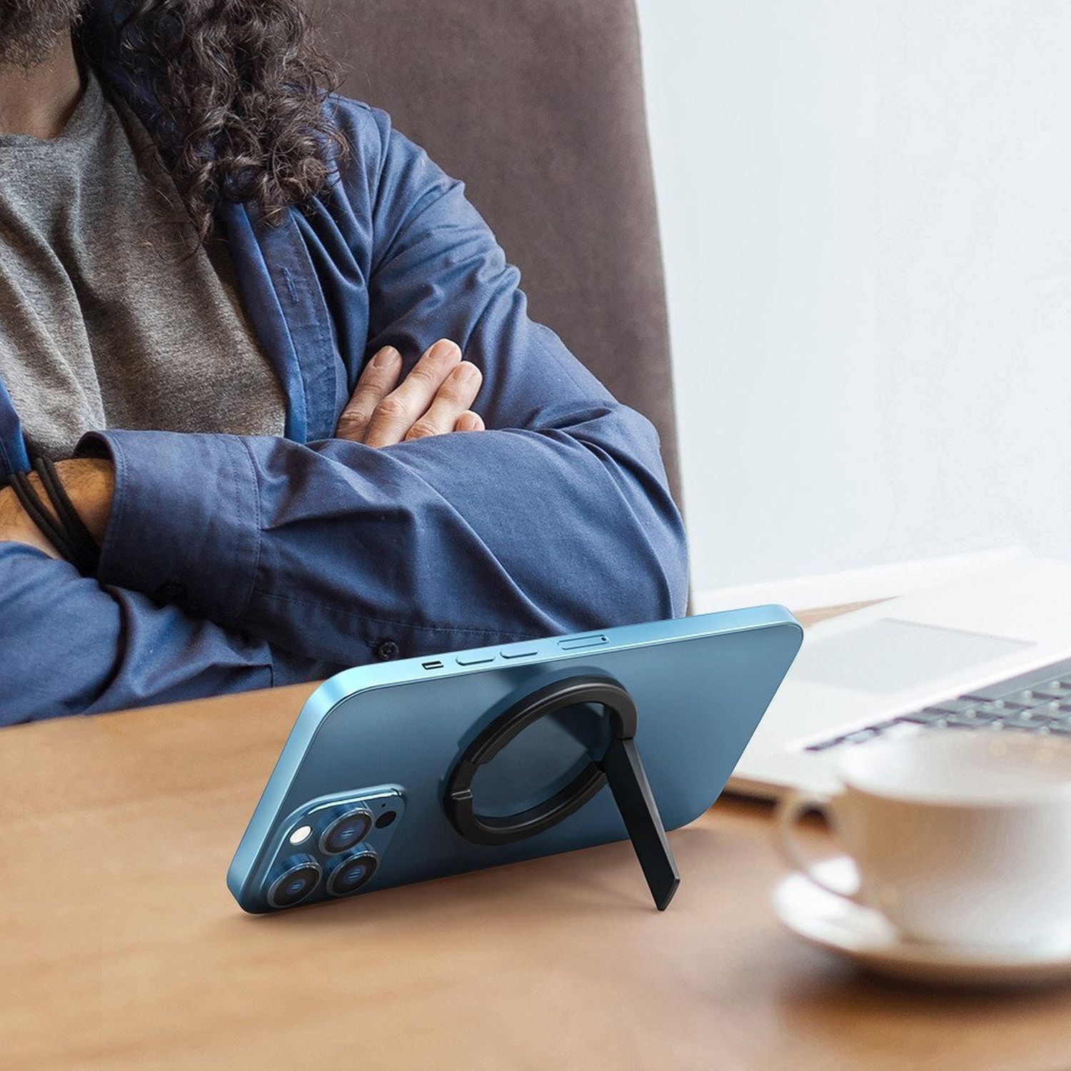 Blaues Telefon mit einem magnetischen Ringständer. Das Telefon steht auf einem Tisch in der Nähe eines Laptops und einer Tasse.