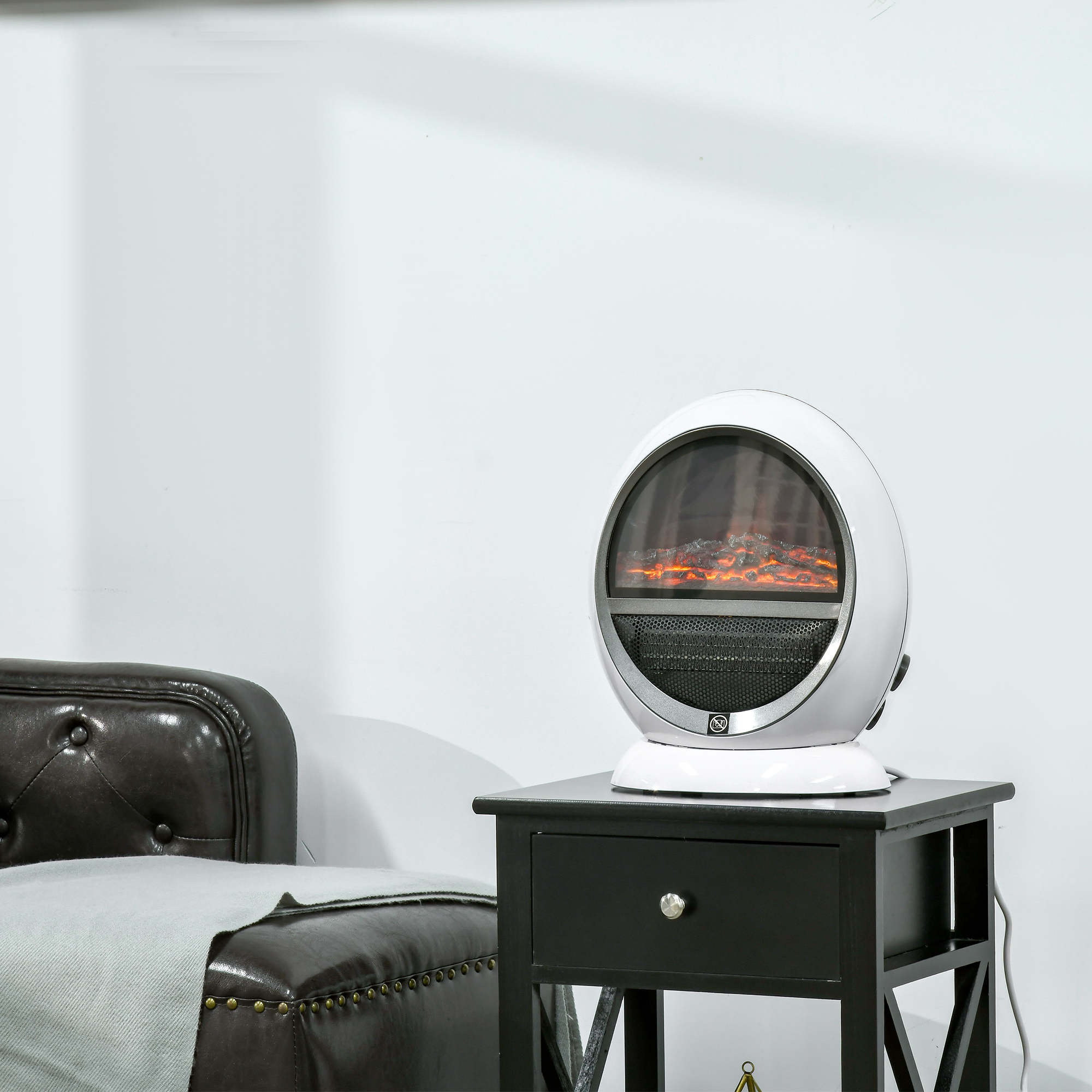 Un caminetto elettrico bianco di forma ovale, con un tavolo nero e una coperta grigia davanti a un muro bianco.
