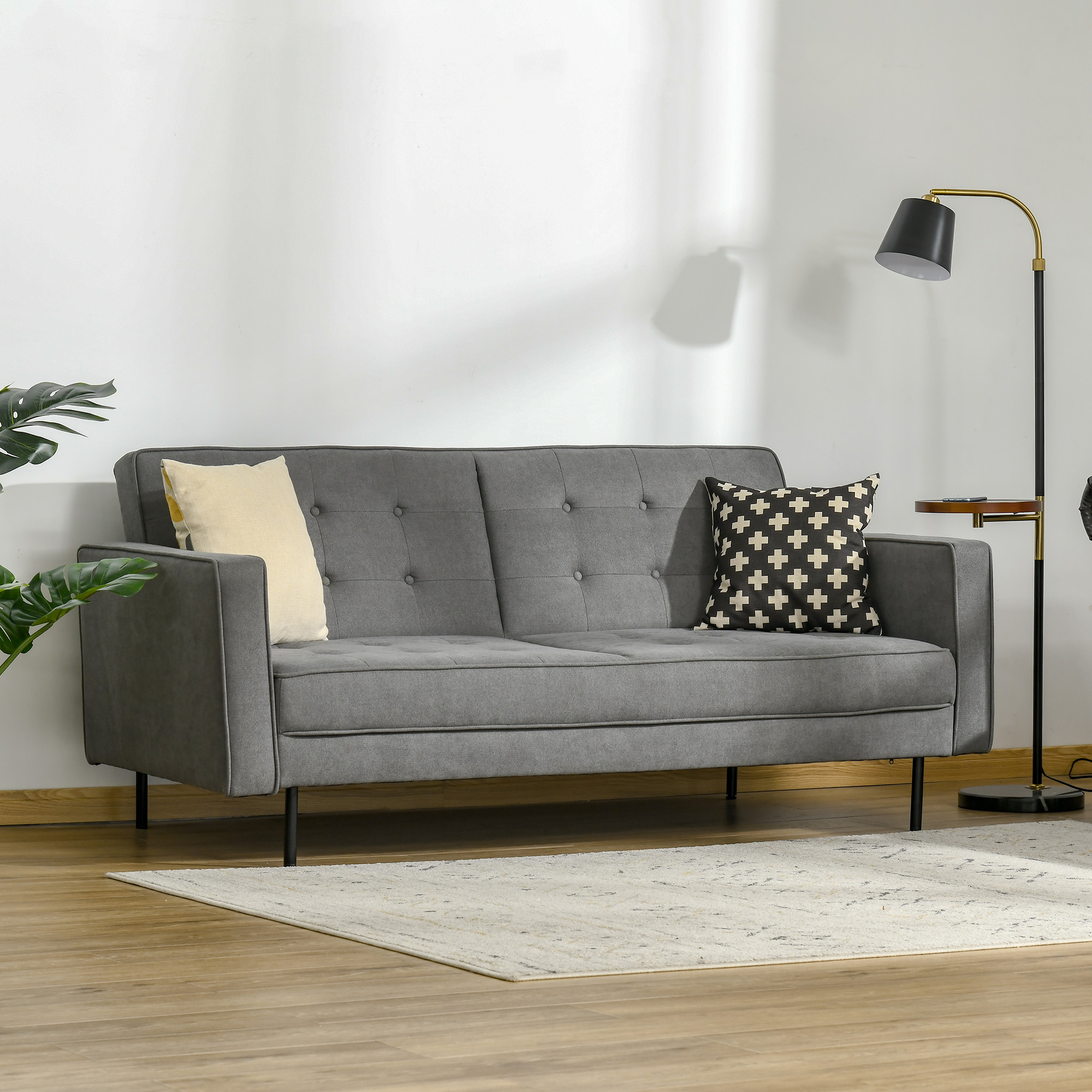 Graues Sofa mit Kissen, einem Teppich und einer Lampe. Links ist eine Pflanze. Die Szene ist in einem Raum.