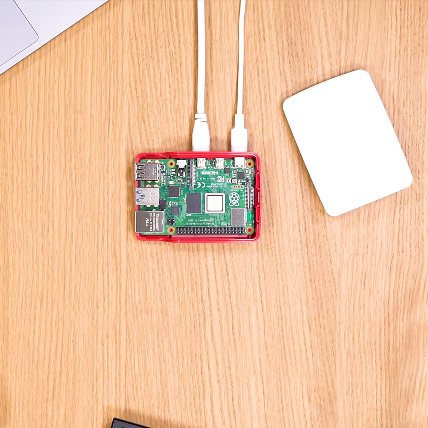 Ein Raspberry Pi-Board mit rotem Gehäuse, verbunden mit einem Laptop und einem weißen Gerät.