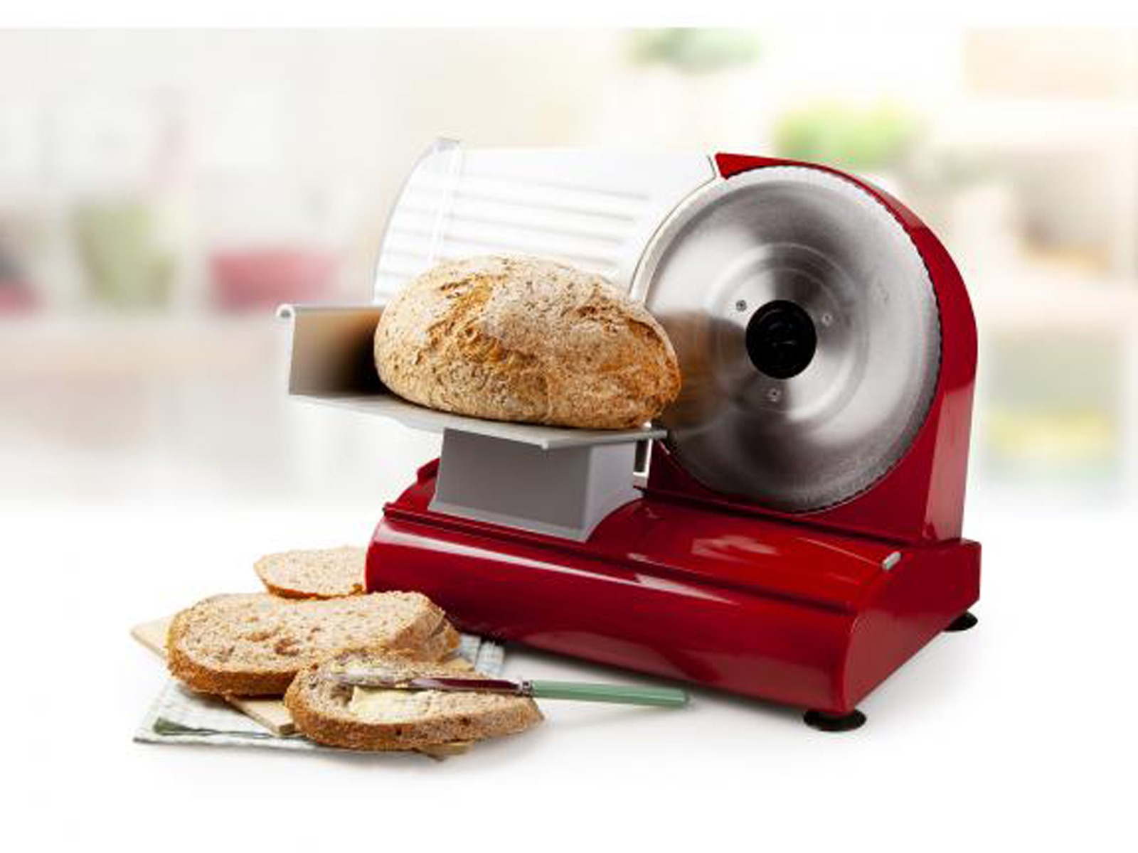 Roter Brotschneider mit Brotlaib und geschnittenem Brot auf einer Oberfläche.