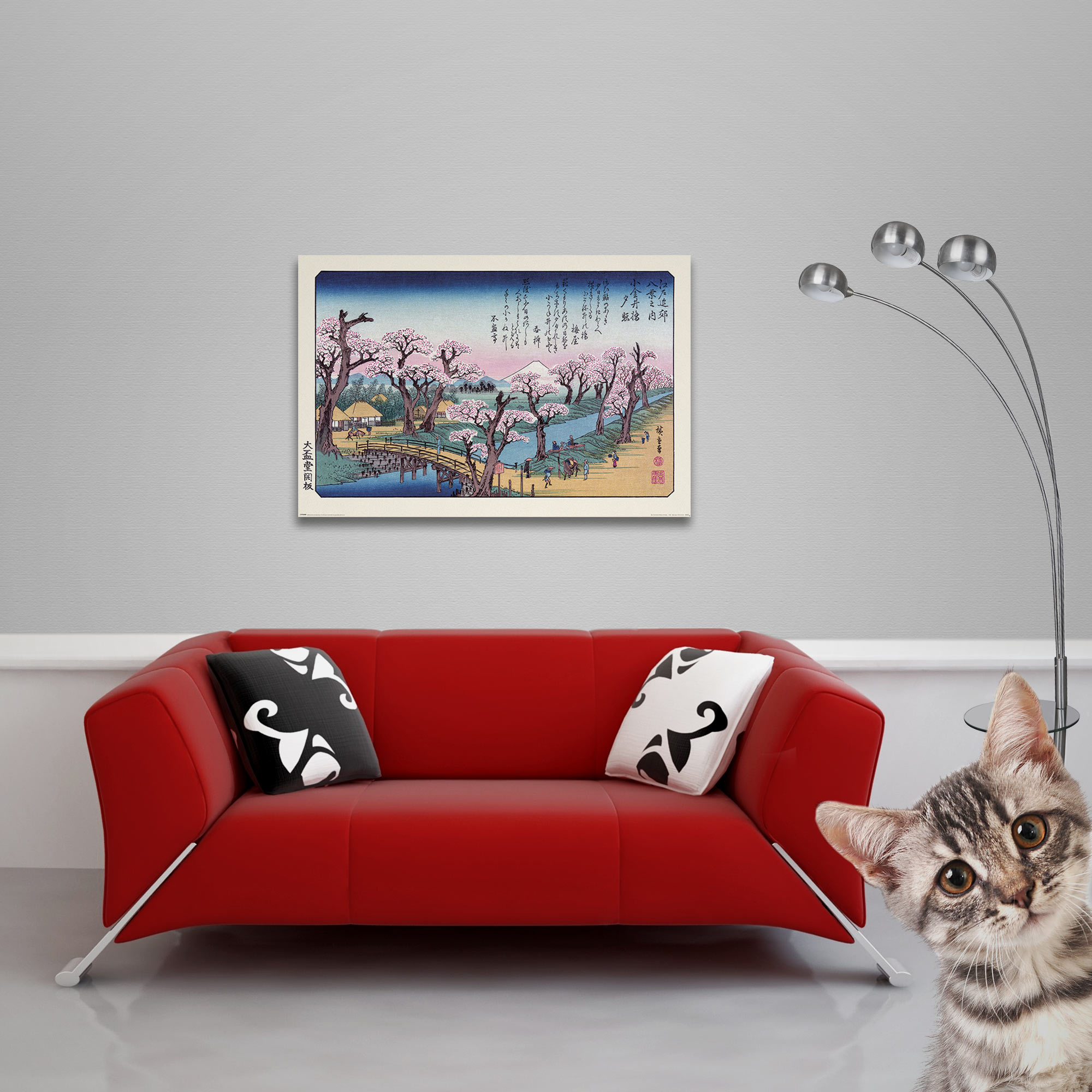 Ein gerahmter japanischer Kunstdruck über einem roten Sofa. Eine Katze blickt von rechts in den Rahmen.