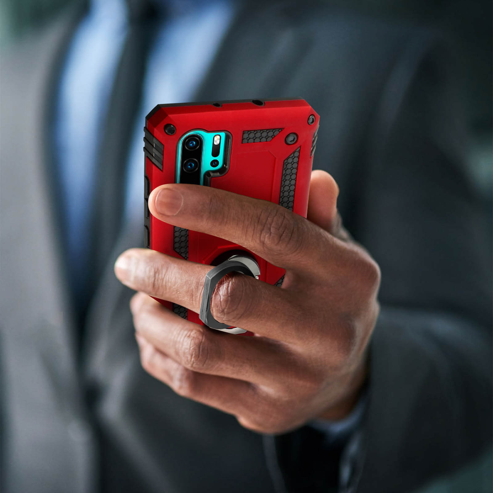 Una mano che tiene una custodia rossa per telefono con un anello per fotocamera e uno sfondo nero.