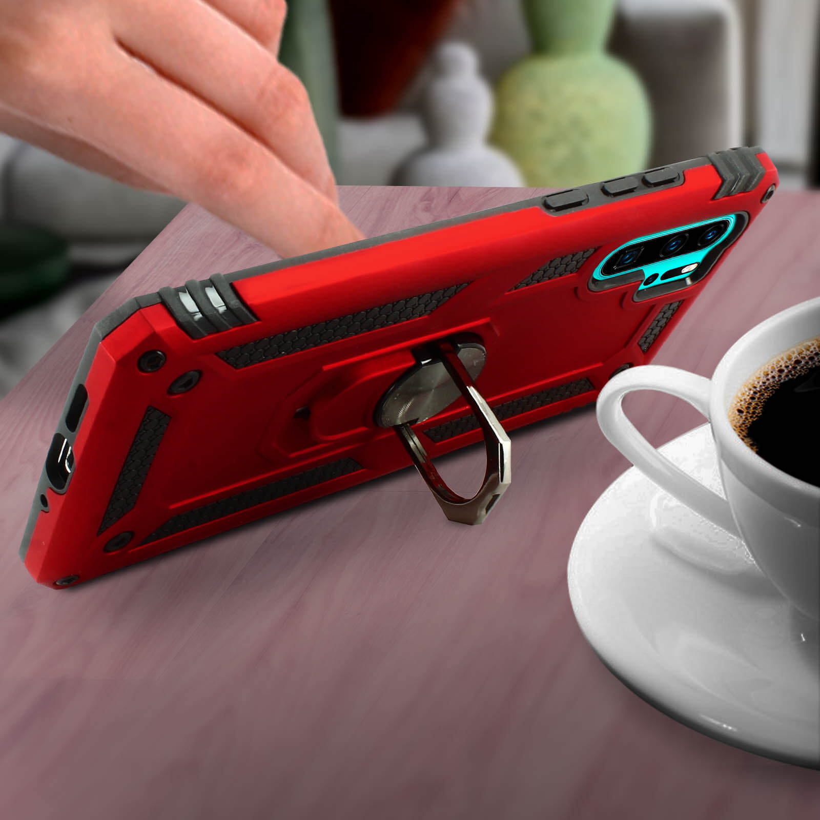 Custodia rossa con anello su tavolo in legno accanto a tazza e piattino di caffè.