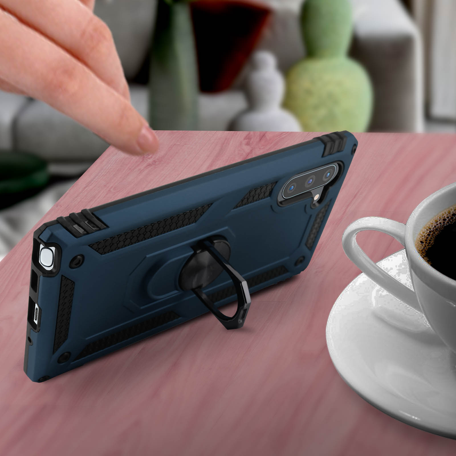 Una custodia per telefono blu con un supporto ad anello su un tavolo di legno accanto a una tazza di caffè.