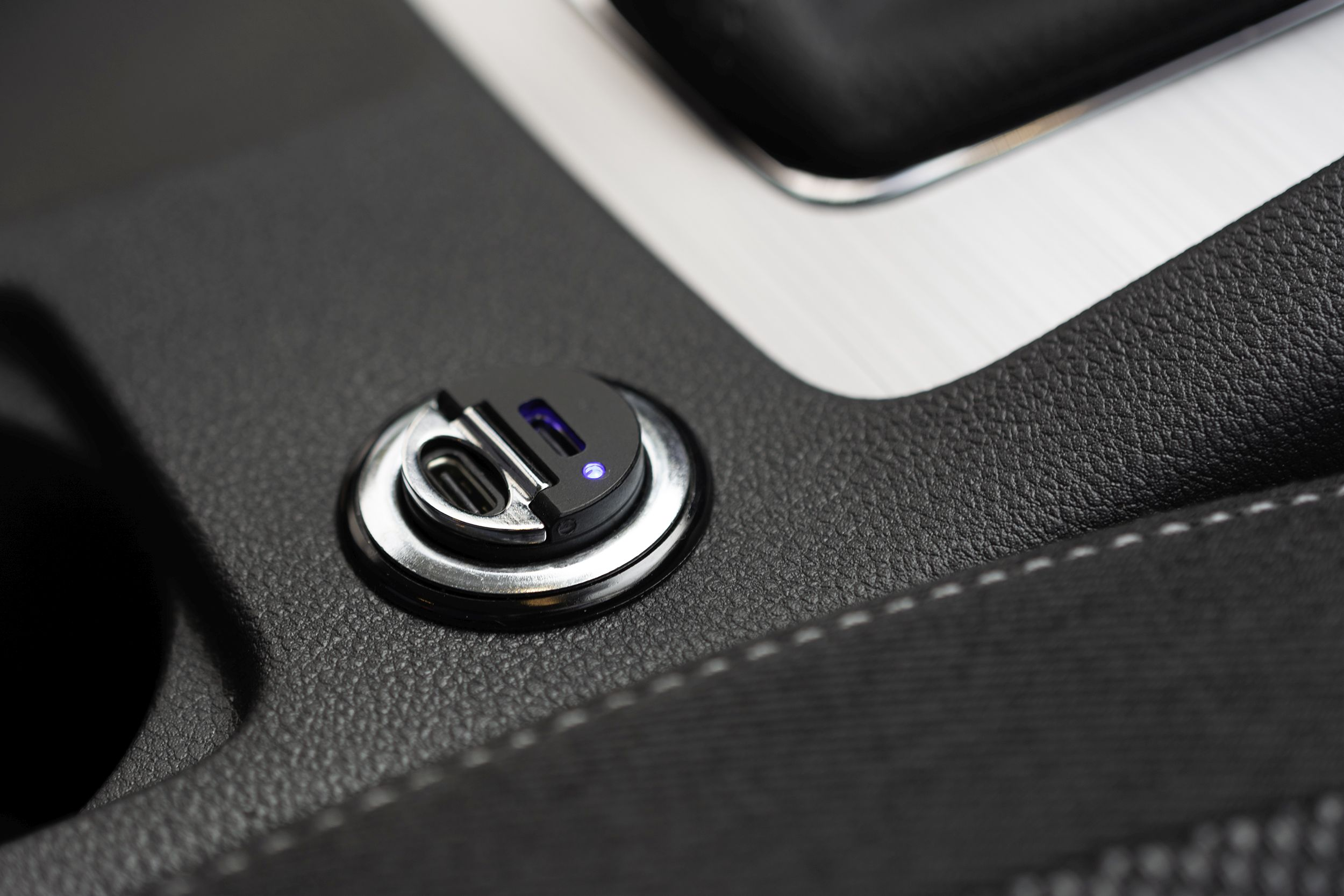 Ein USB-C-Autoladegerät. Es ist schwarz mit einem silbernen Ring und einem blauen Licht.