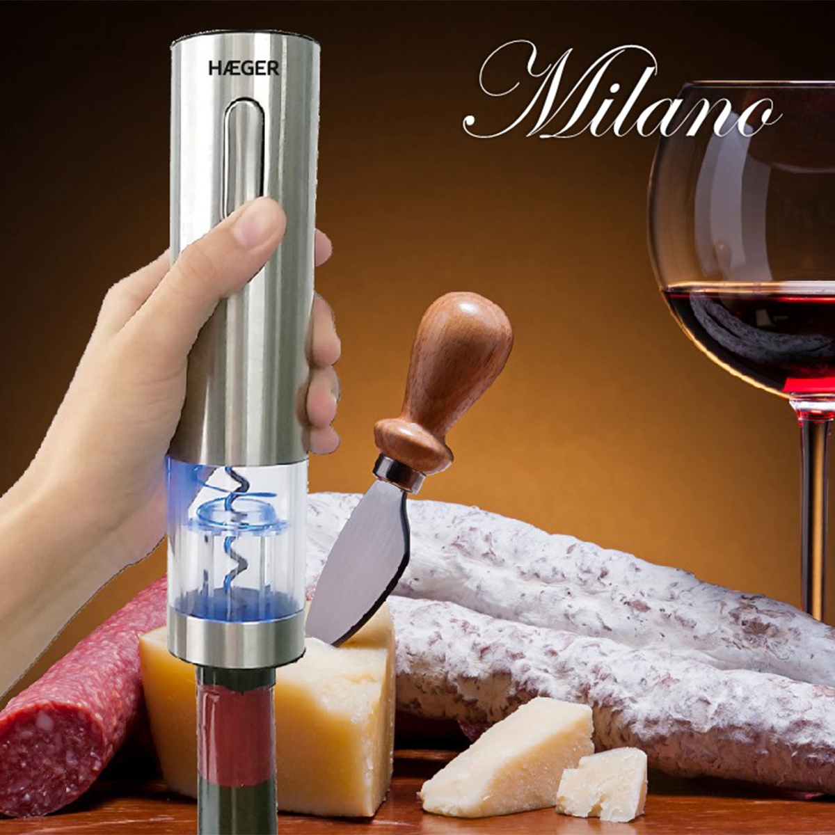 Mano sosteniendo abridor de vino eléctrico sobre botella de vino tinto, con queso, salami y copa de vino al fondo.