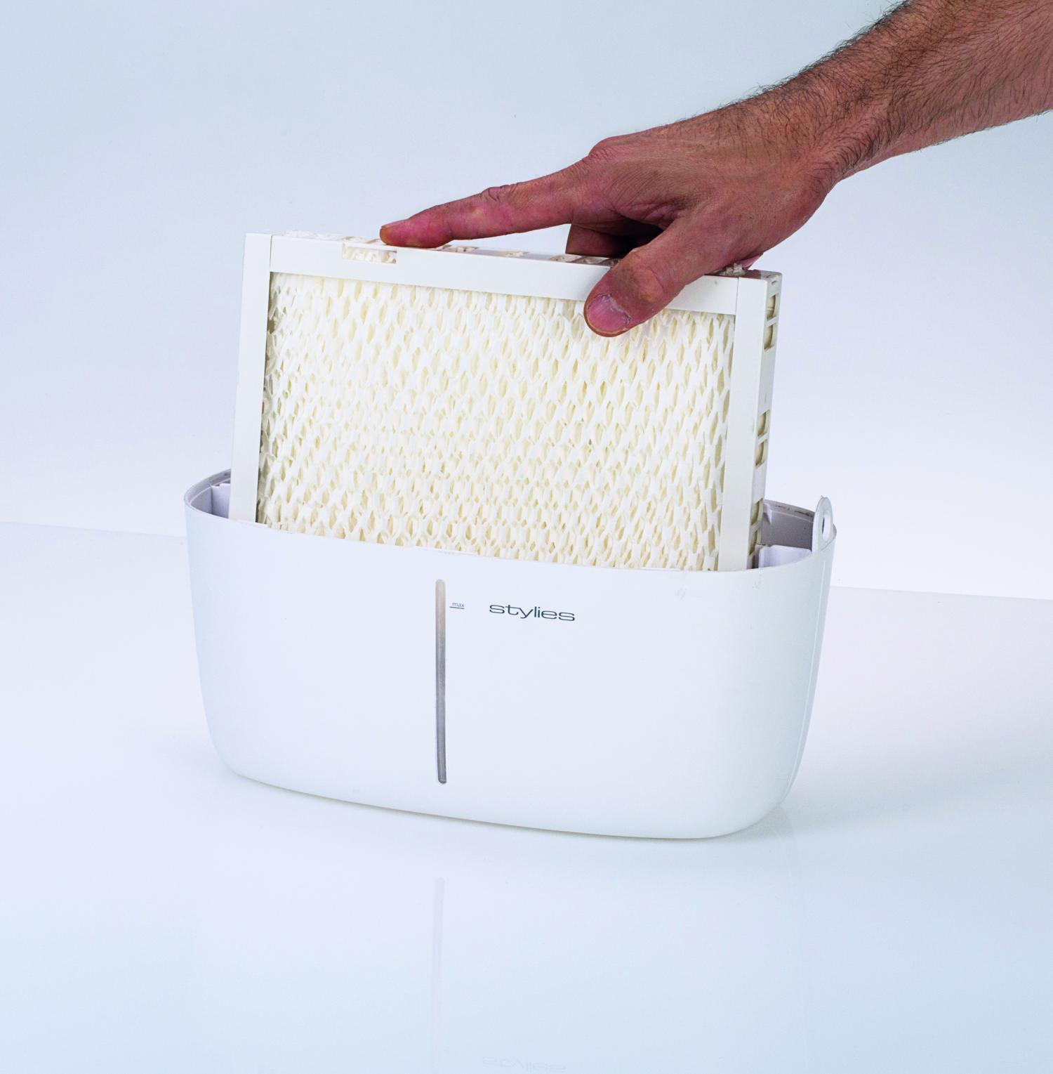 Una mano inserta un filtro blanco en un humidificador blanco. El humidificador tiene un indicador de nivel de agua.