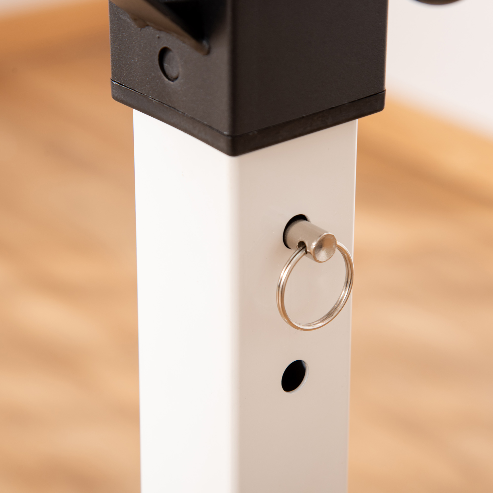 Primer plano de un poste metálico blanco y negro con un anillo plateado. Suelo de madera al fondo.