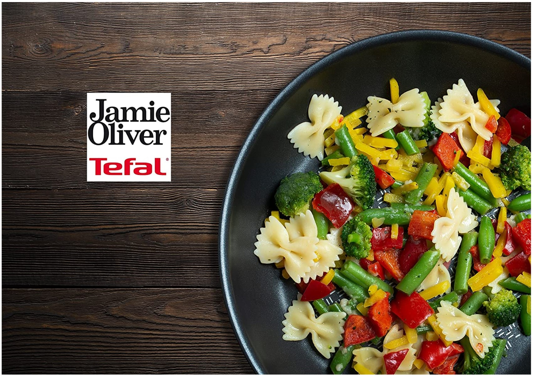 Nudeln und Gemüse in einer Pfanne auf einem Holztisch. Jamie Oliver und Tefal Logo in der Ecke.