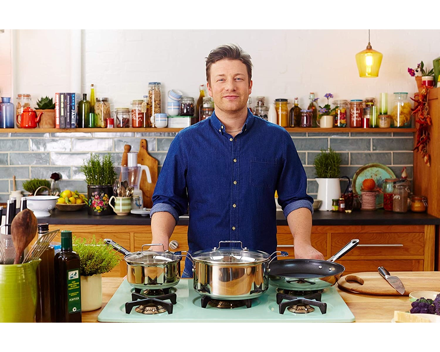 Jamie Oliver in einer Küche, lächelnd, mit Töpfen auf dem Herd und Zutaten.