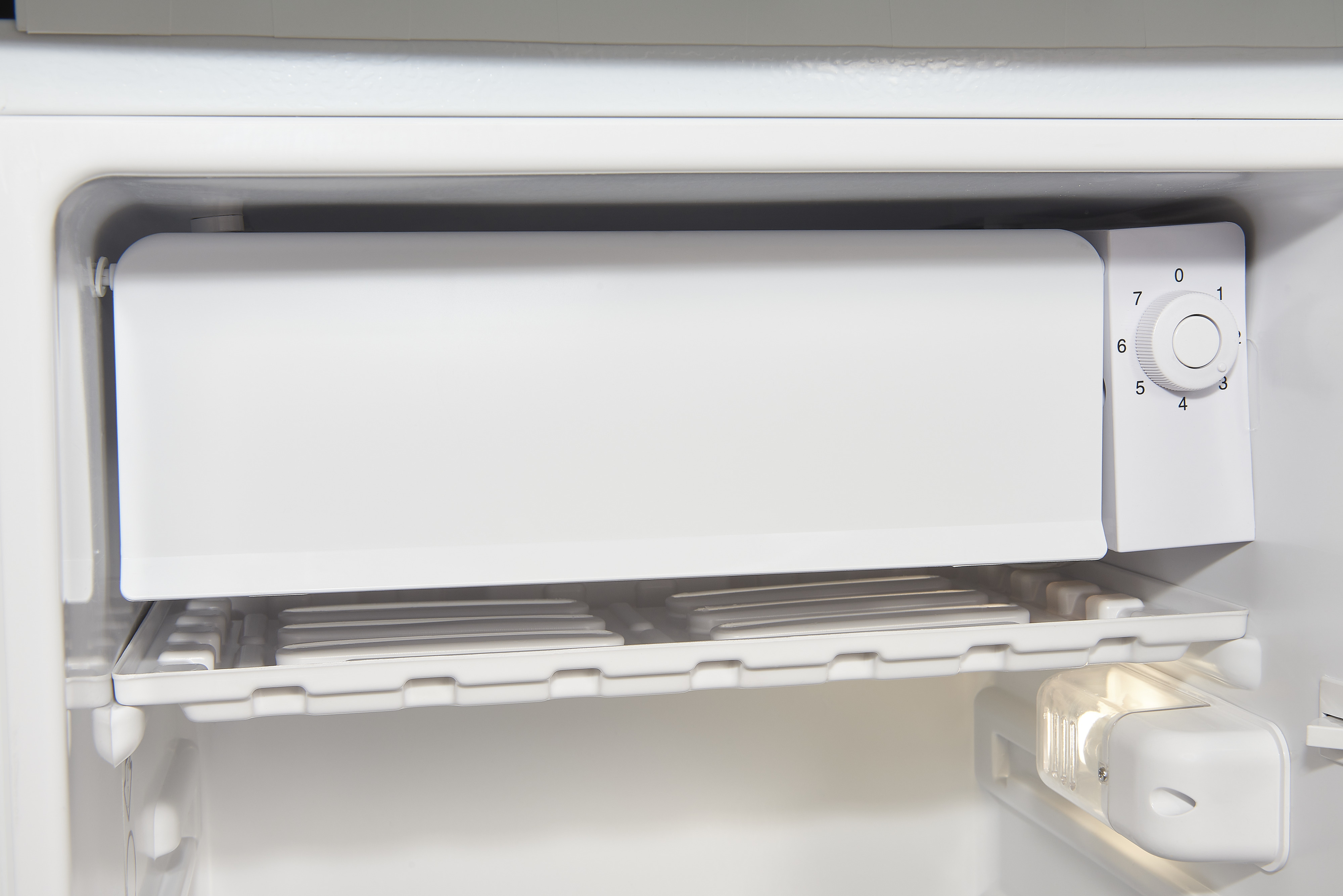 Innenseite eines weißen Kühlschranks mit Regalen und einem Temperaturregelrad.