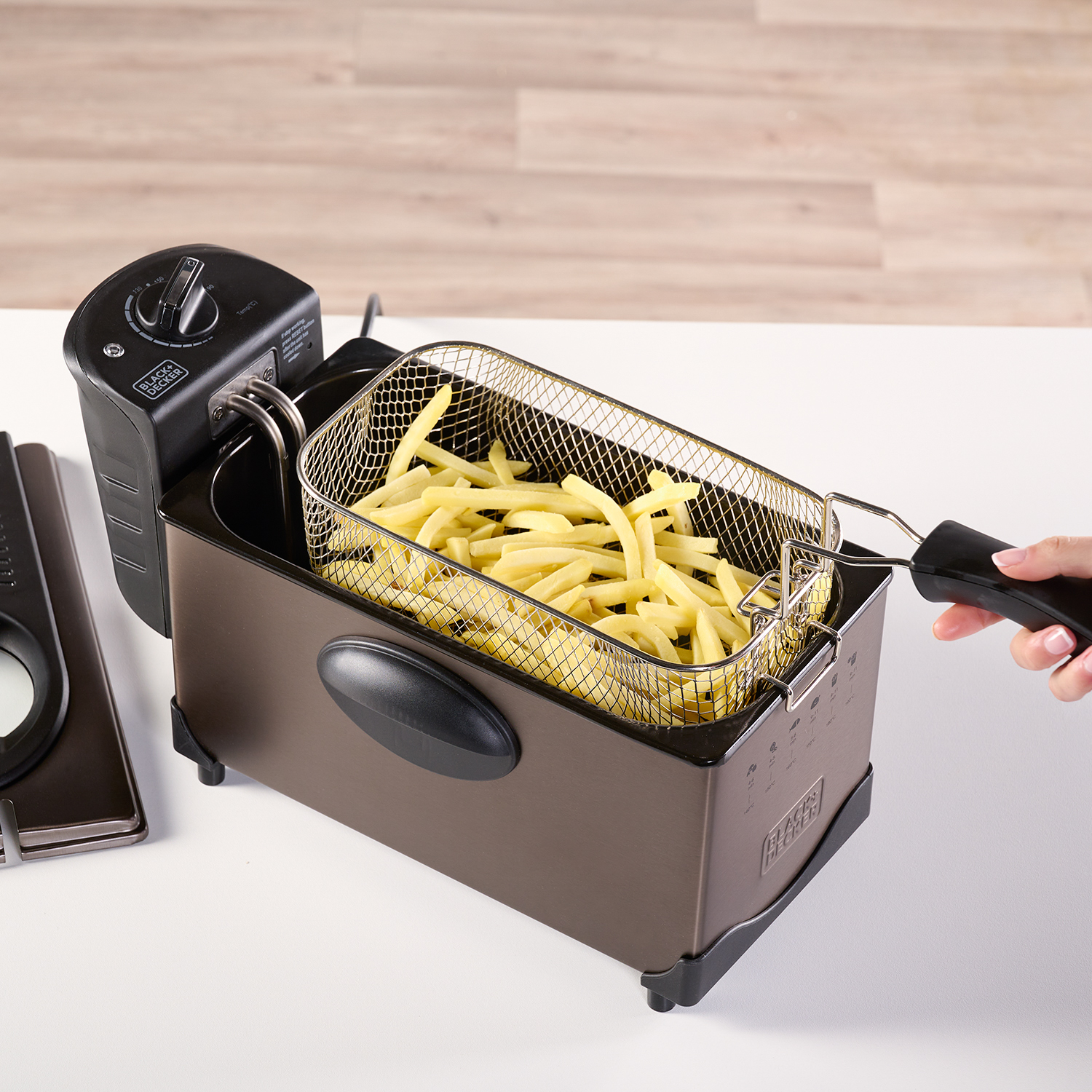 Frytownica z frytkami w koszyku i dłonią trzymającą uchwyt.