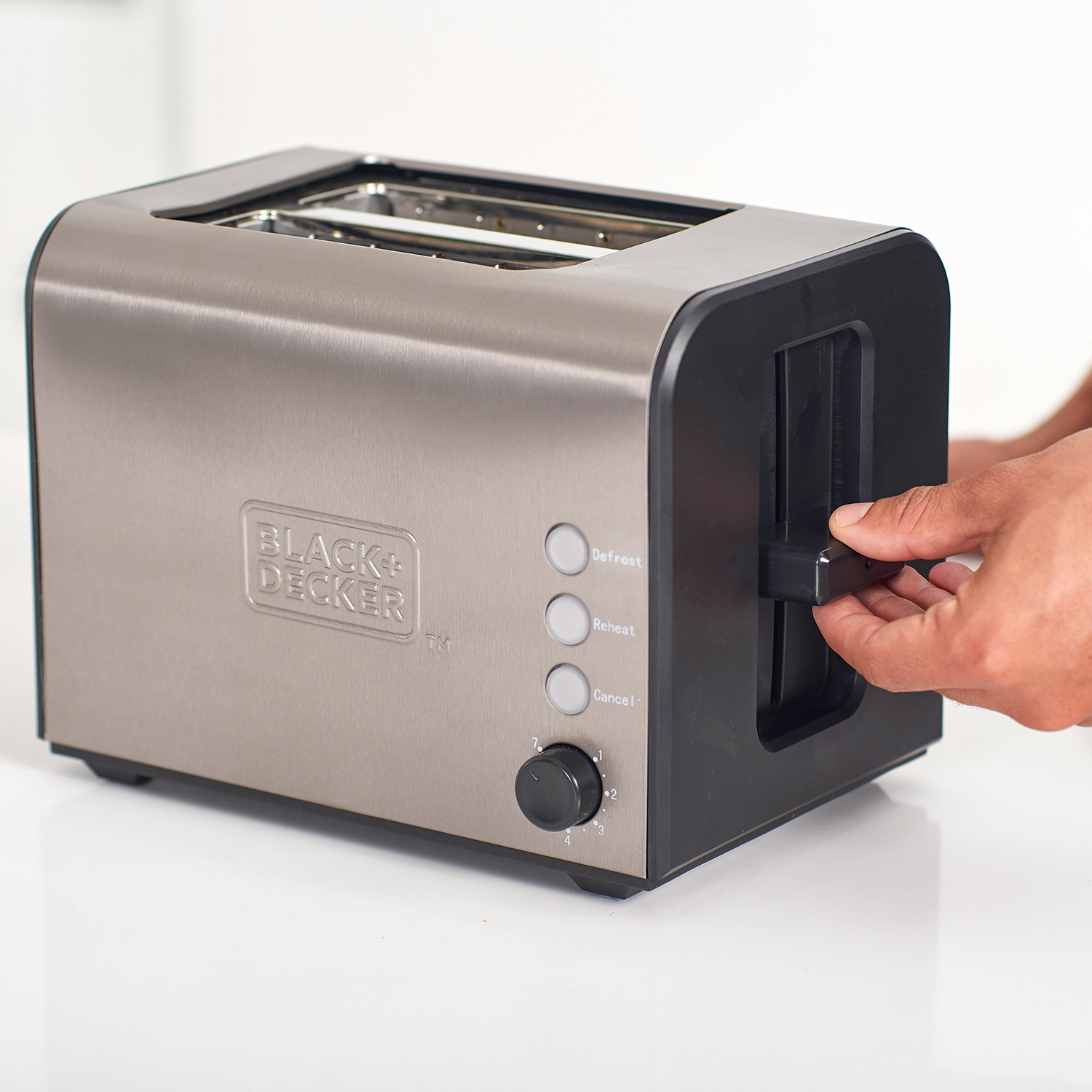 Srebrny i czarny toster z przyciskami i dźwignią na białej powierzchni. Ręka reguluje dźwignię.