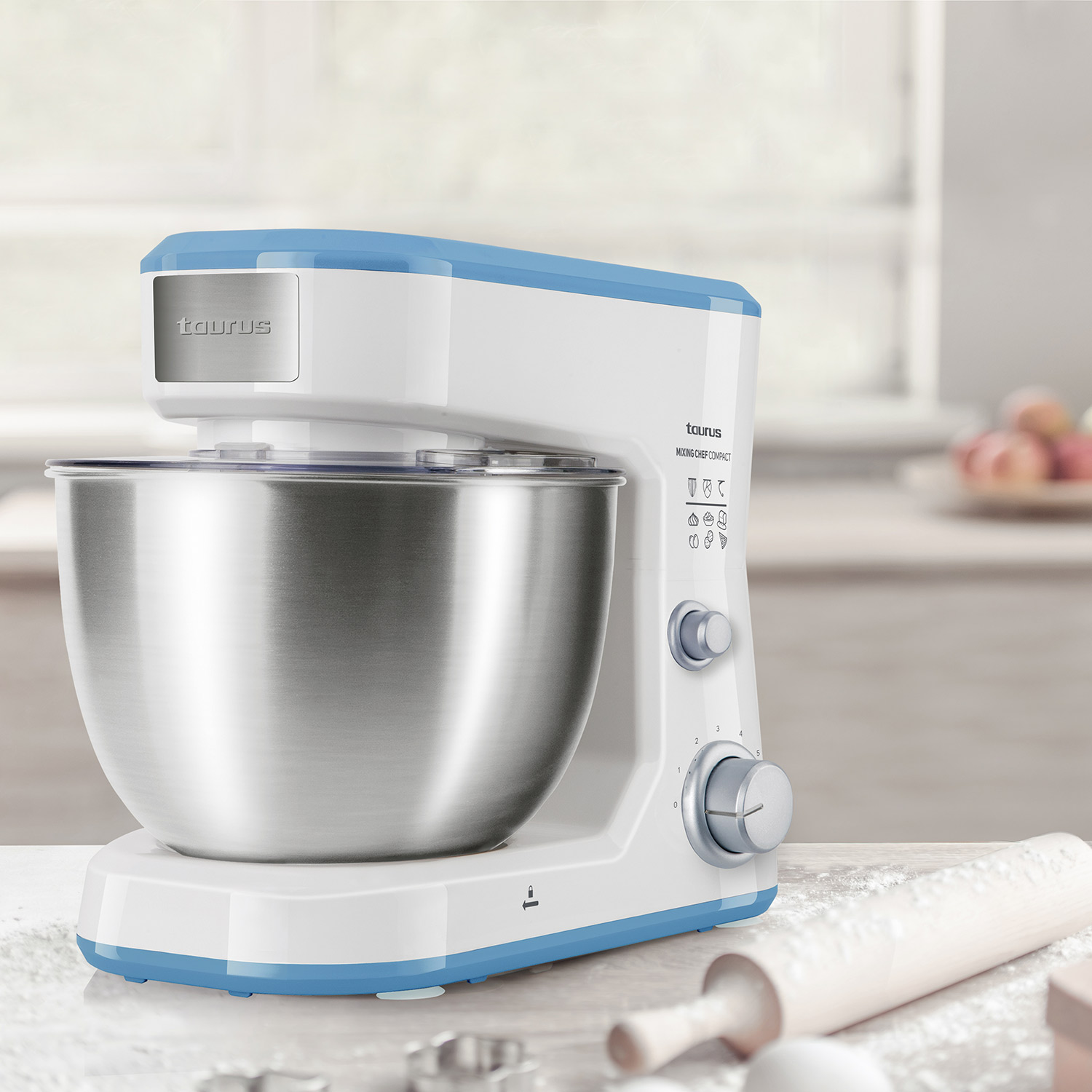 Un robot da cucina Taurus bianco e blu, con una ciotola in acciaio inossidabile, su un piano di lavoro della cucina con utensili.
