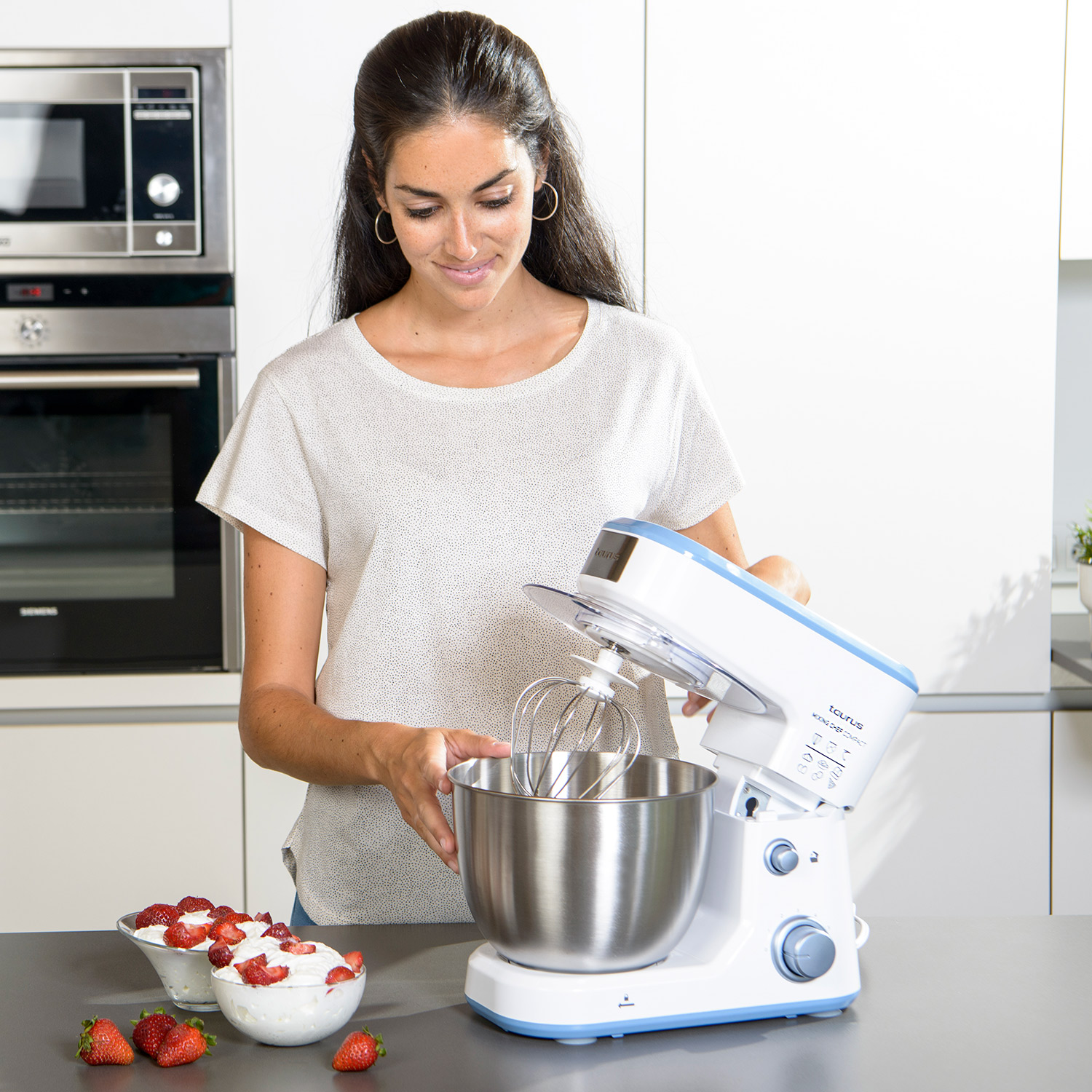 Una donna sta usando un mixer da banco bianco e blu, con una ciotola di fragole accanto a lei.