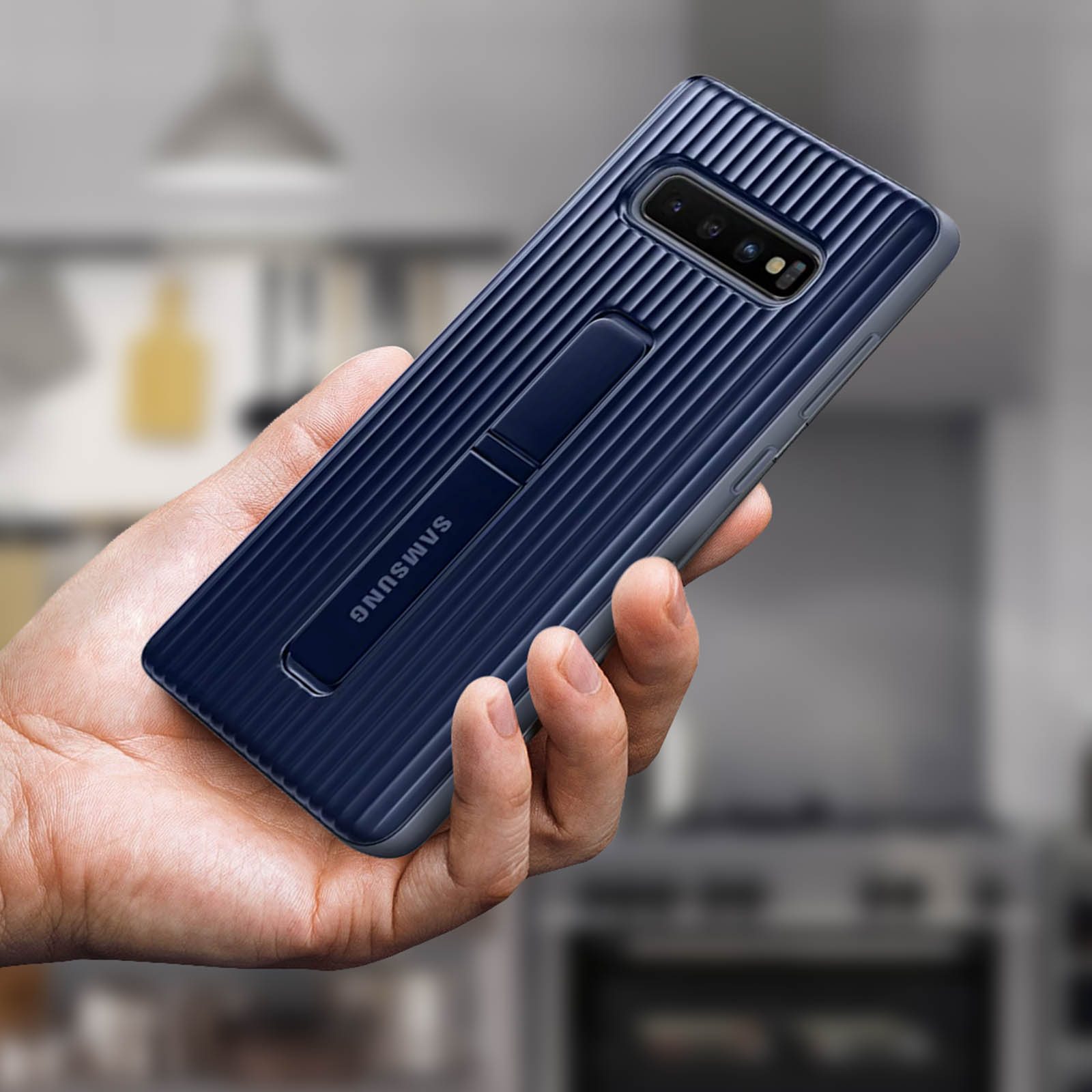 Telefoon in de hand, marineblauw. De telefoon heeft een standaard en een camera. De achtergrond is wazig.