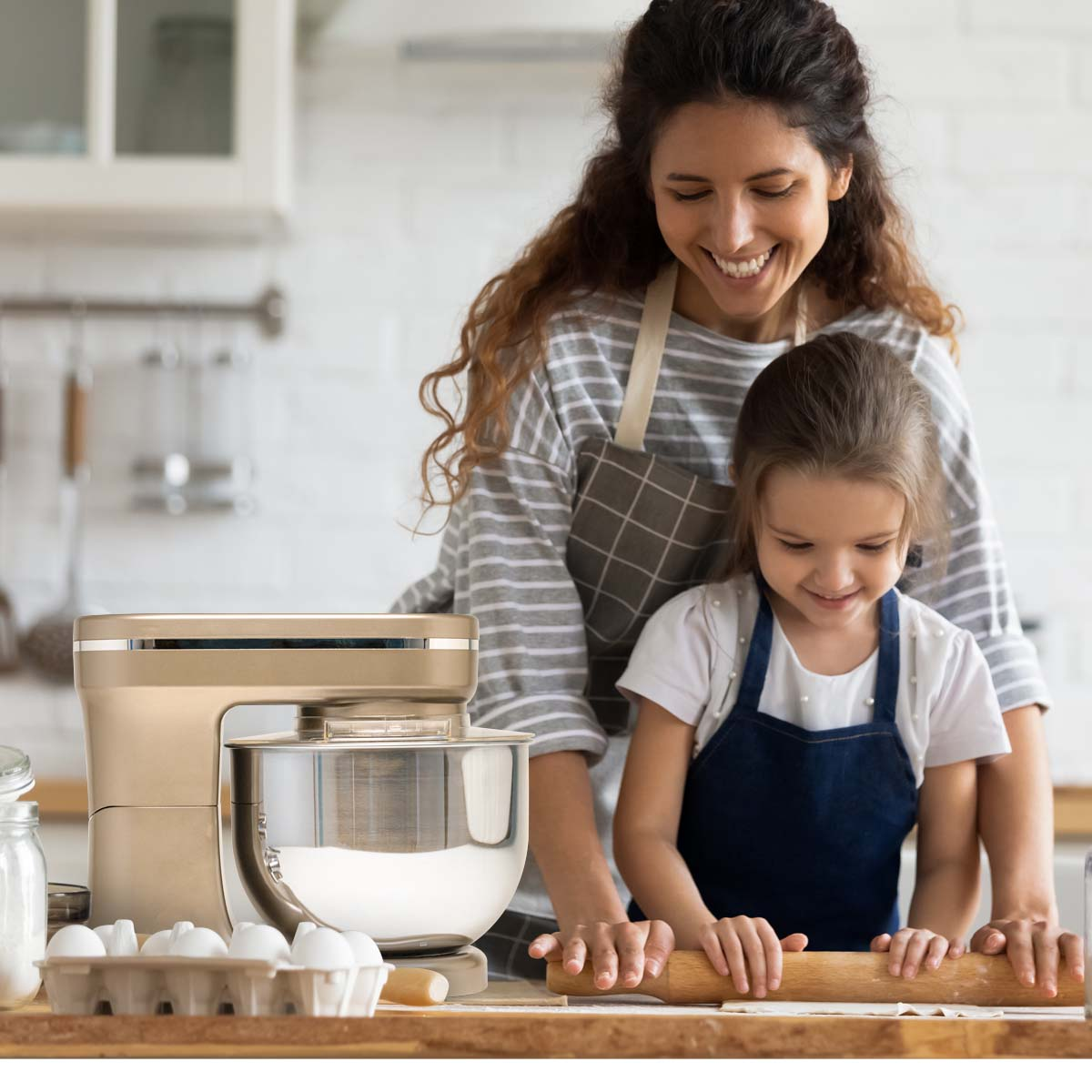 Woman and child baking with a beige stand mixer and eggs. Kitchen background.