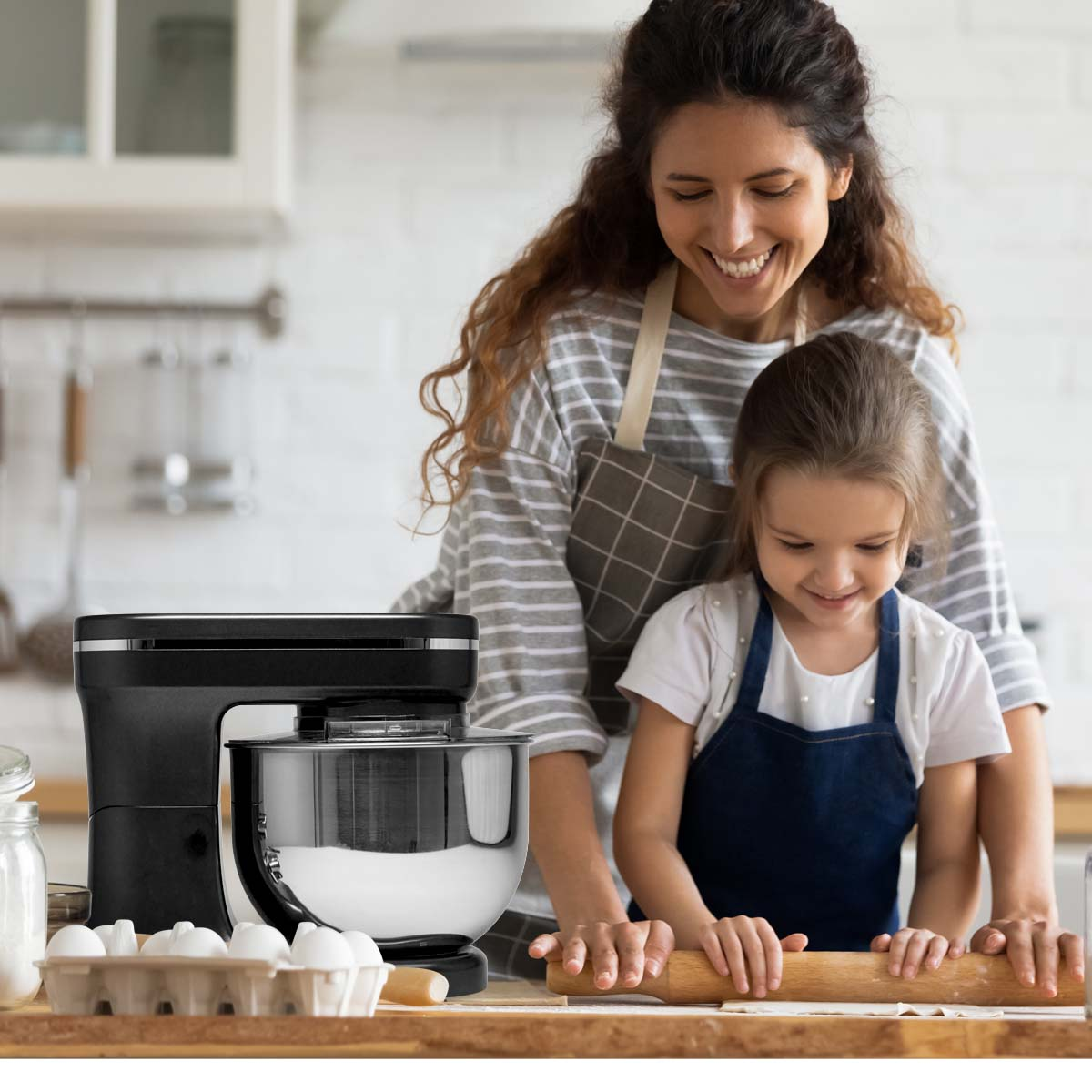 Woman and girl in kitchen. They are using a mixer. Eggs and bowl of flour are visible.