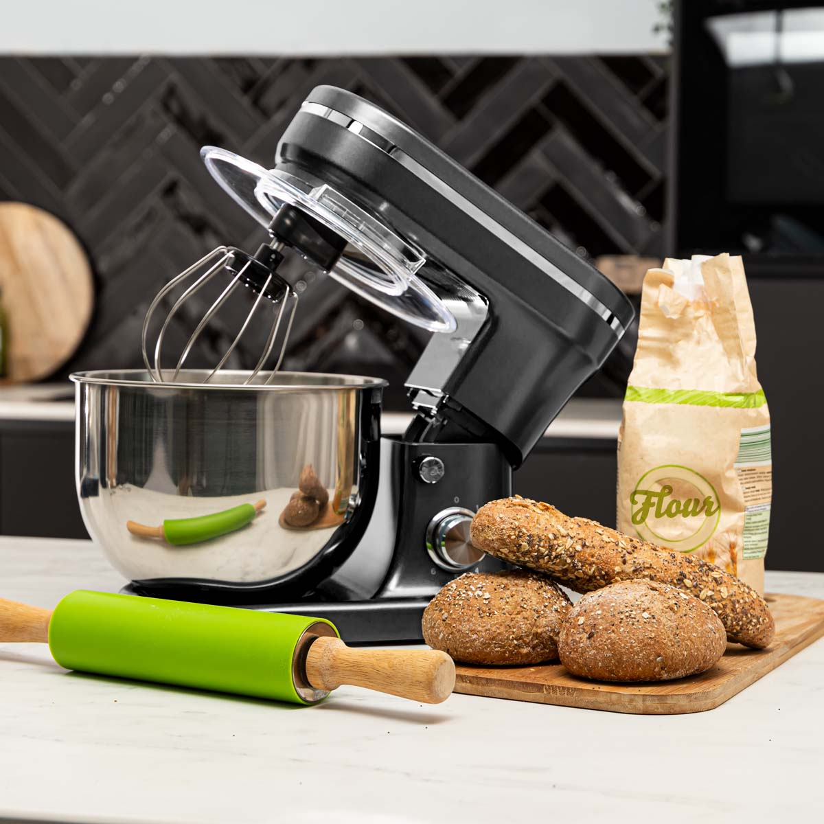 Stand mixer with bowl, whisk, and bread on wooden board. Rolling pin on the left.