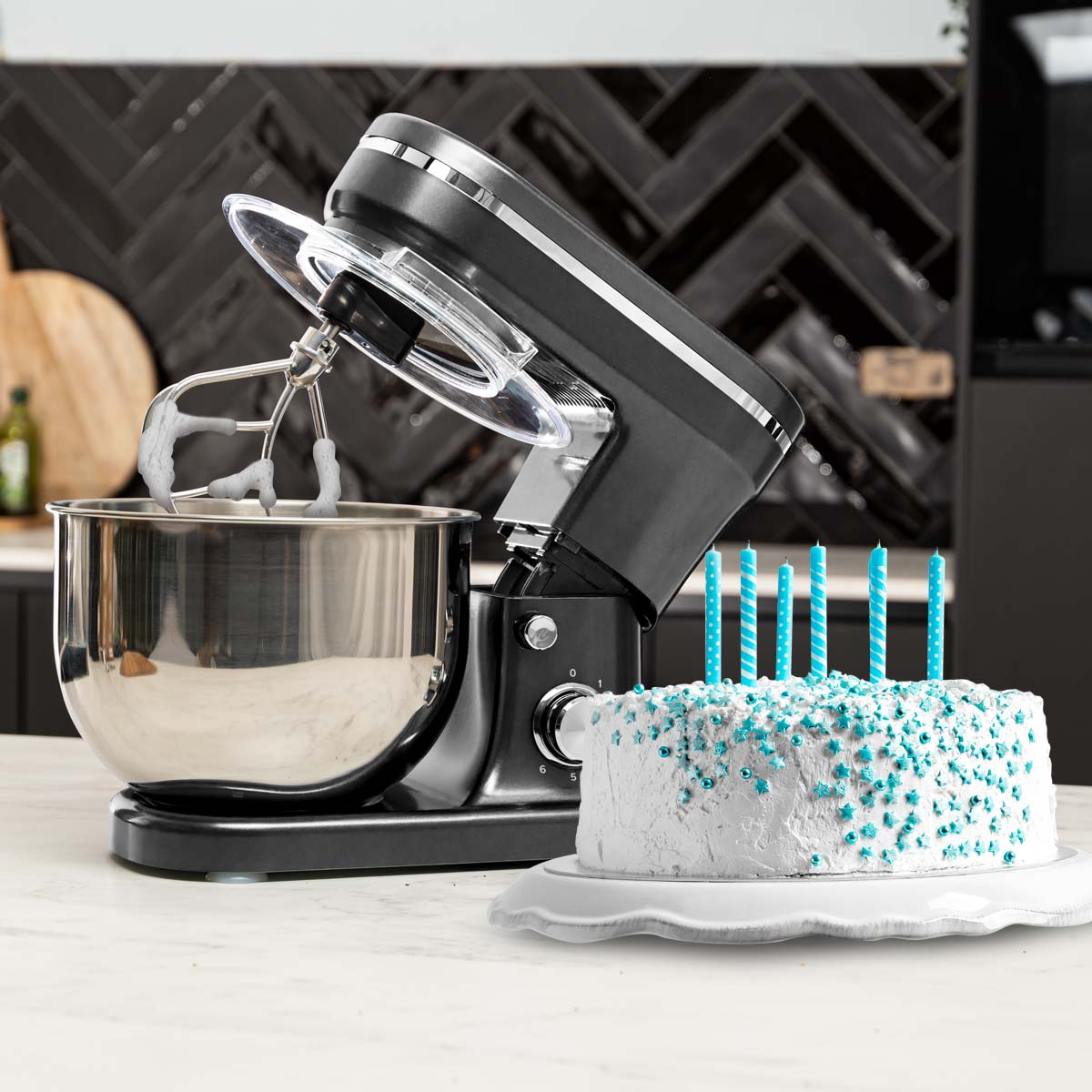 Black stand mixer with a bowl and cake with blue candles. Kitchen background with black tiles.