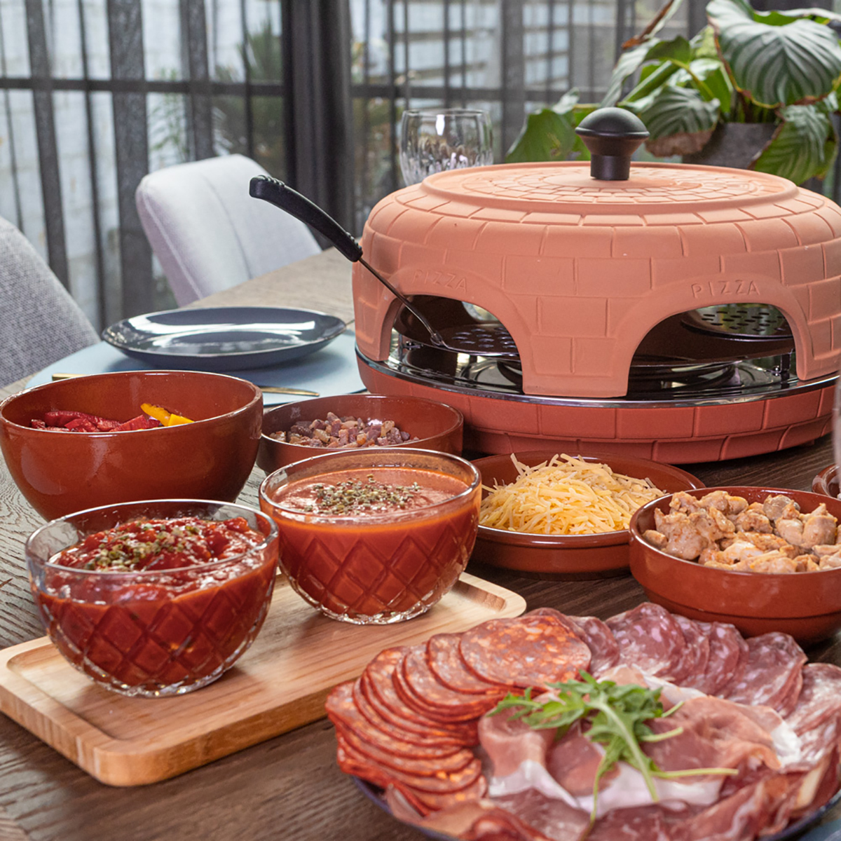 Een tafelsetting met een pizza-oven, ingrediënten en gerechten. De pizza-oven staat in het midden.