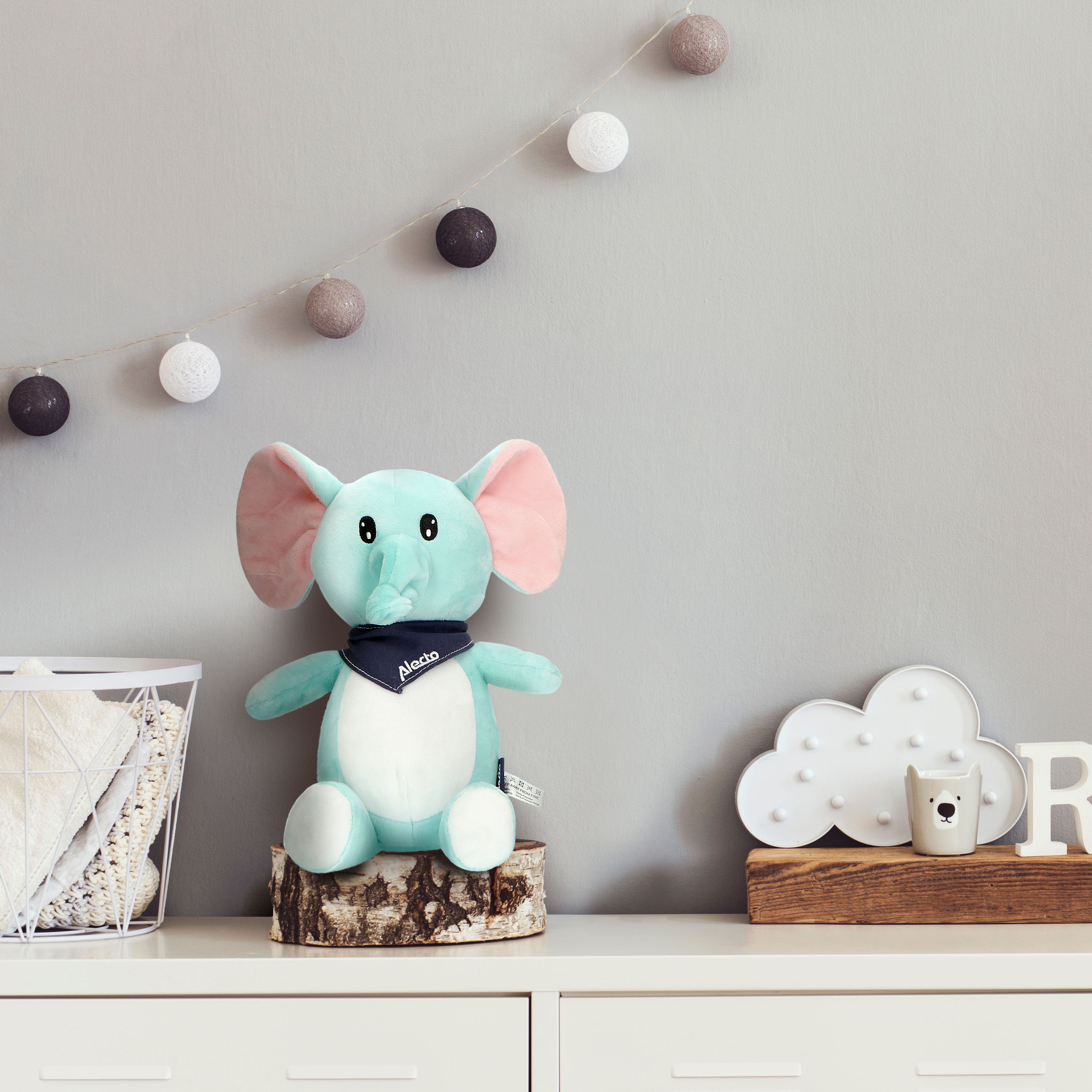 Olifantenknuffel op een stam. Guirlande en andere items op een witte kast.
