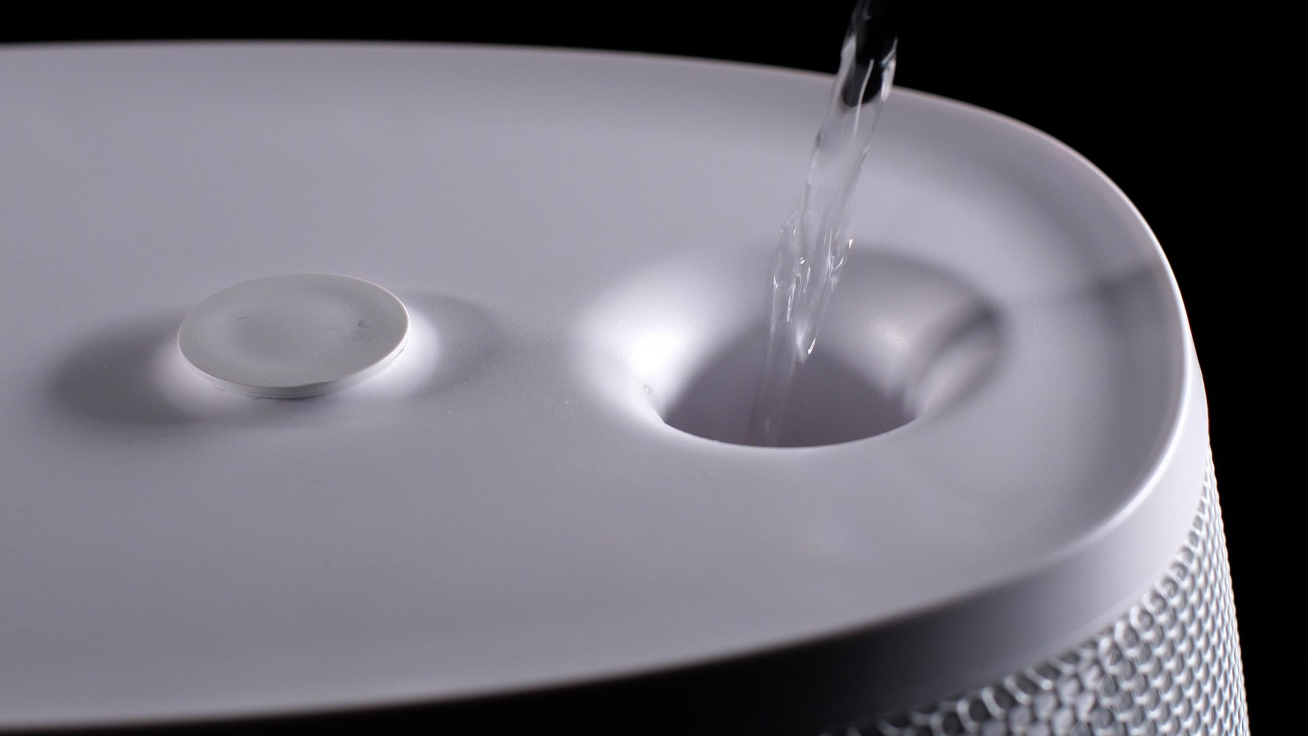 Acqua che viene versata in un dispositivo bianco. Il dispositivo ha una parte superiore rotonda con un foro.
