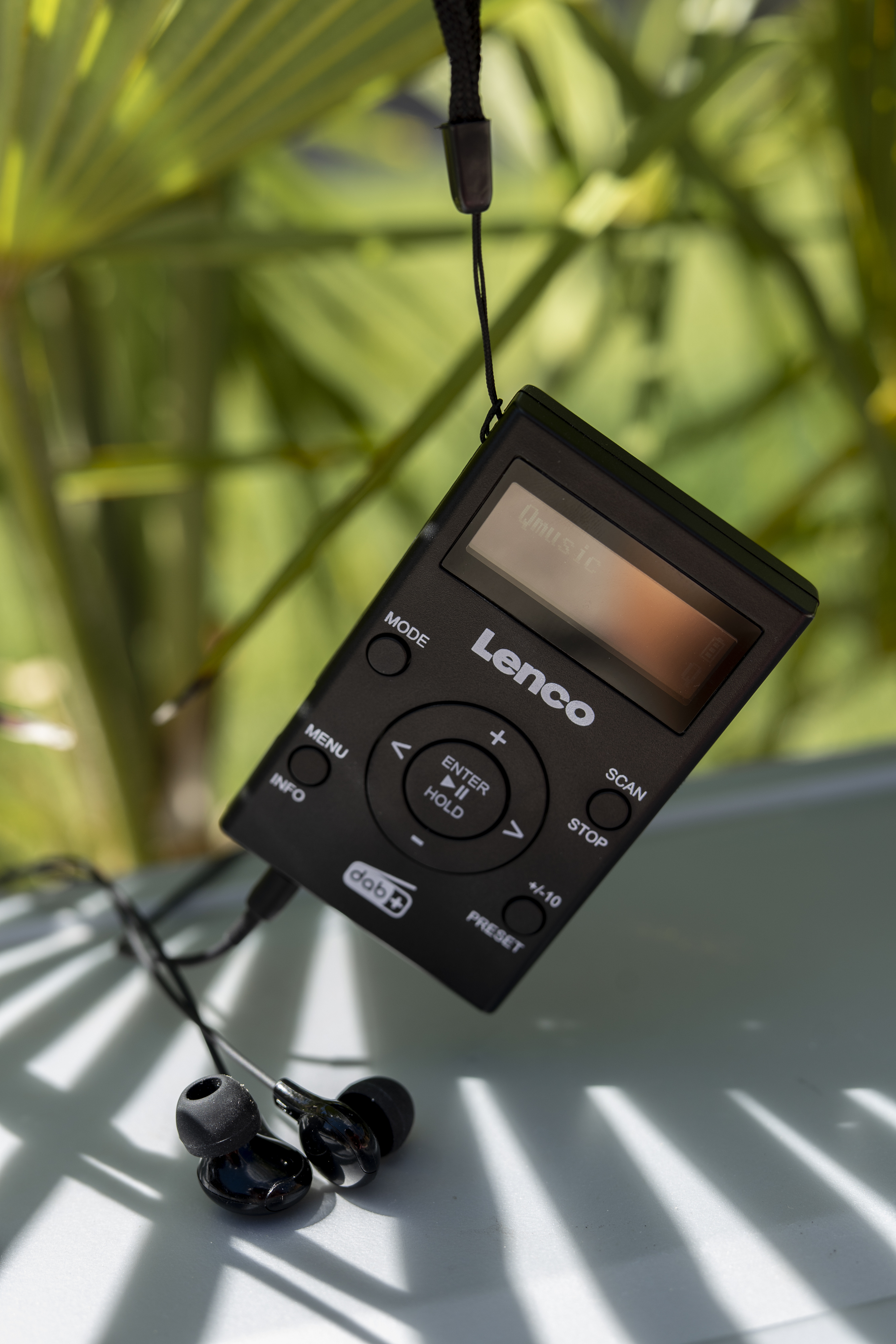 Schwarzes Lenco DAB+ Radio mit Bildschirm und Kopfhörern. Es hängt an einem schwarzen Faden.