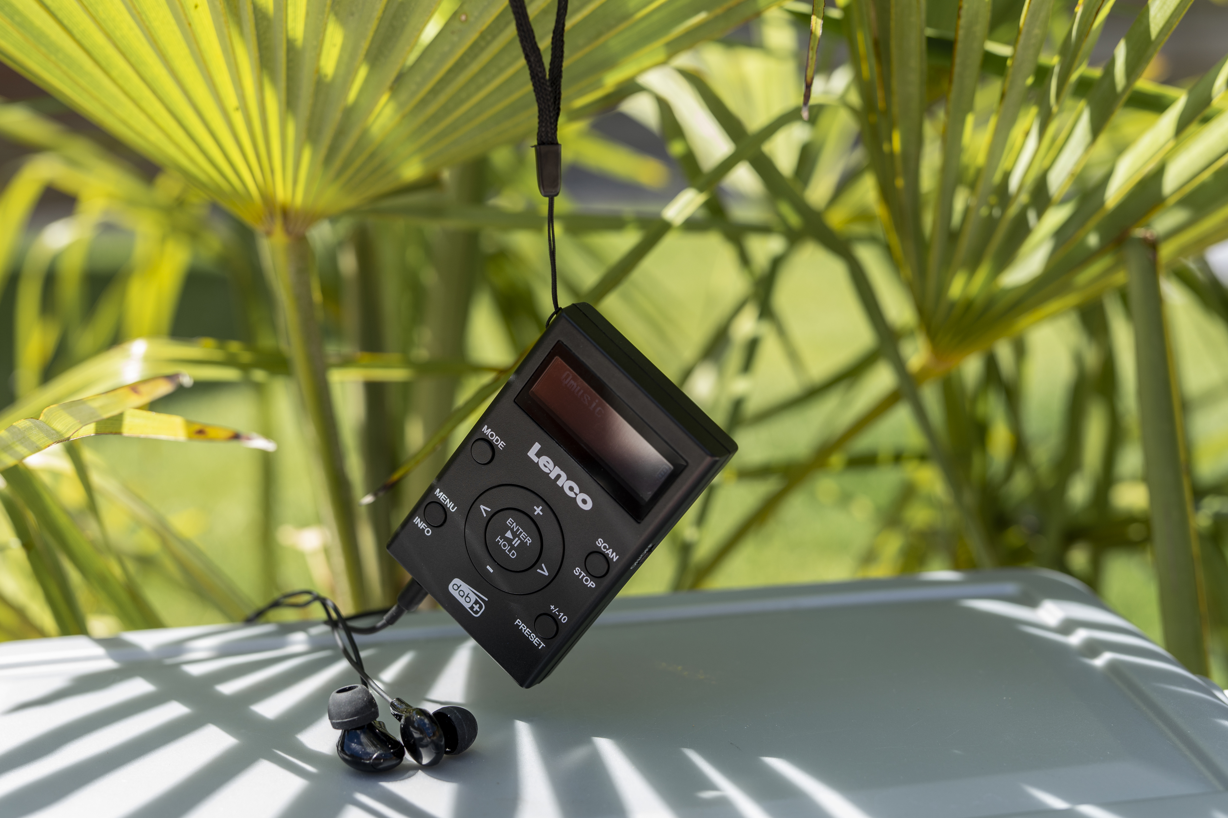 Ein schwarzer Lenco CD-Player mit Kopfhörern, die daran hängen, in der Nähe von grünen Blättern.