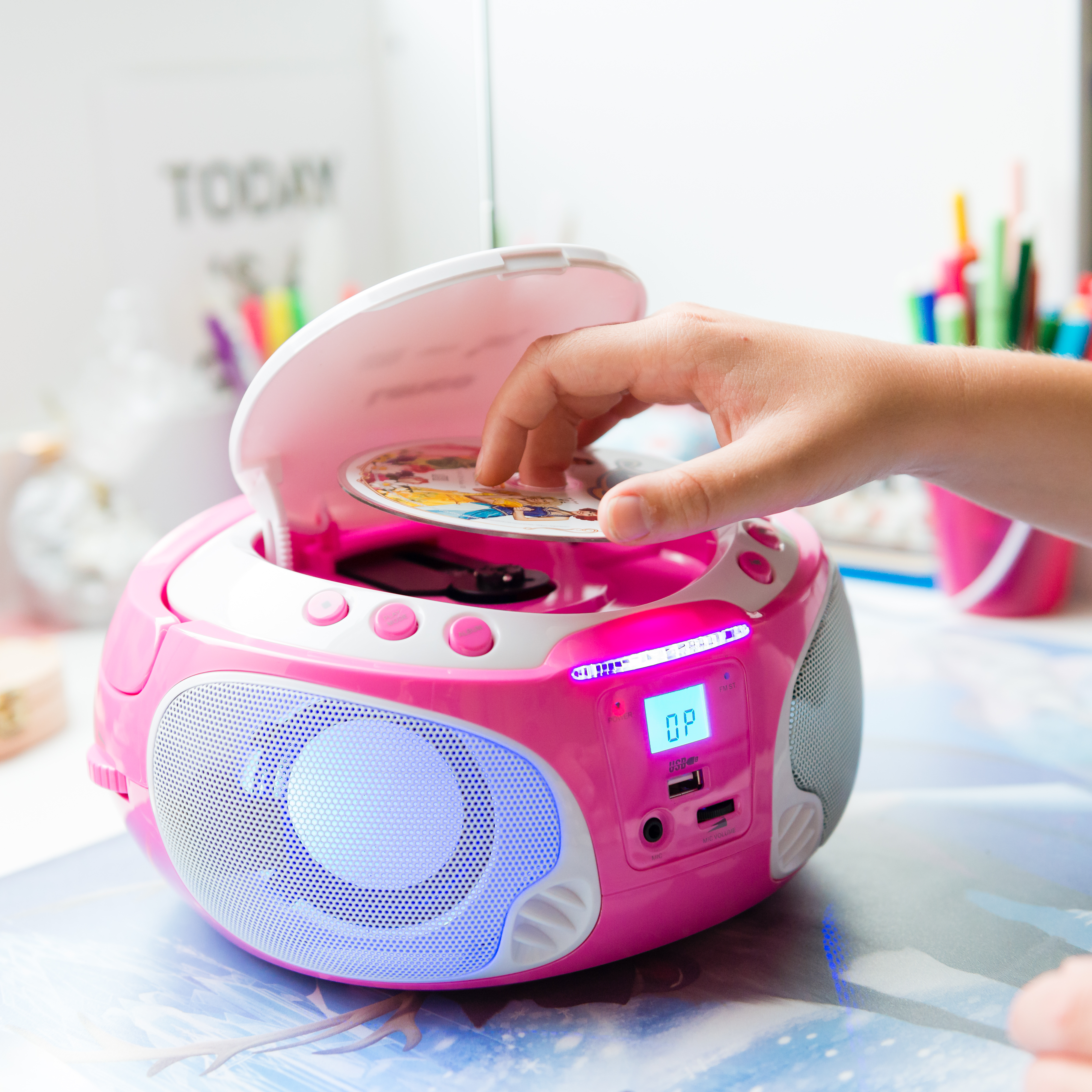 Die Hand eines Kindes legt eine CD in eine rosa-weiße Boombox ein. Der Bildschirm zeigt 'OP'.