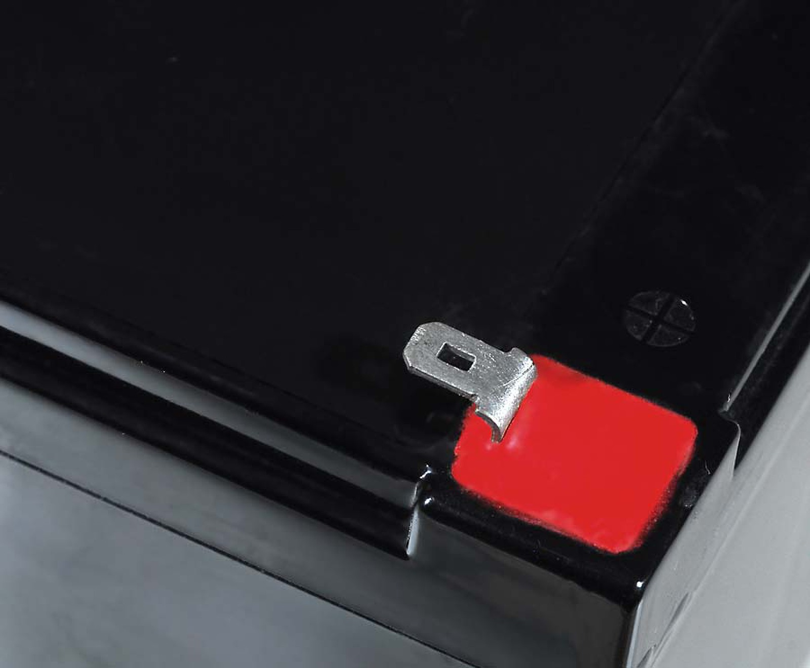 Batería negra con una pegatina roja en el lateral y una lengüeta metálica.