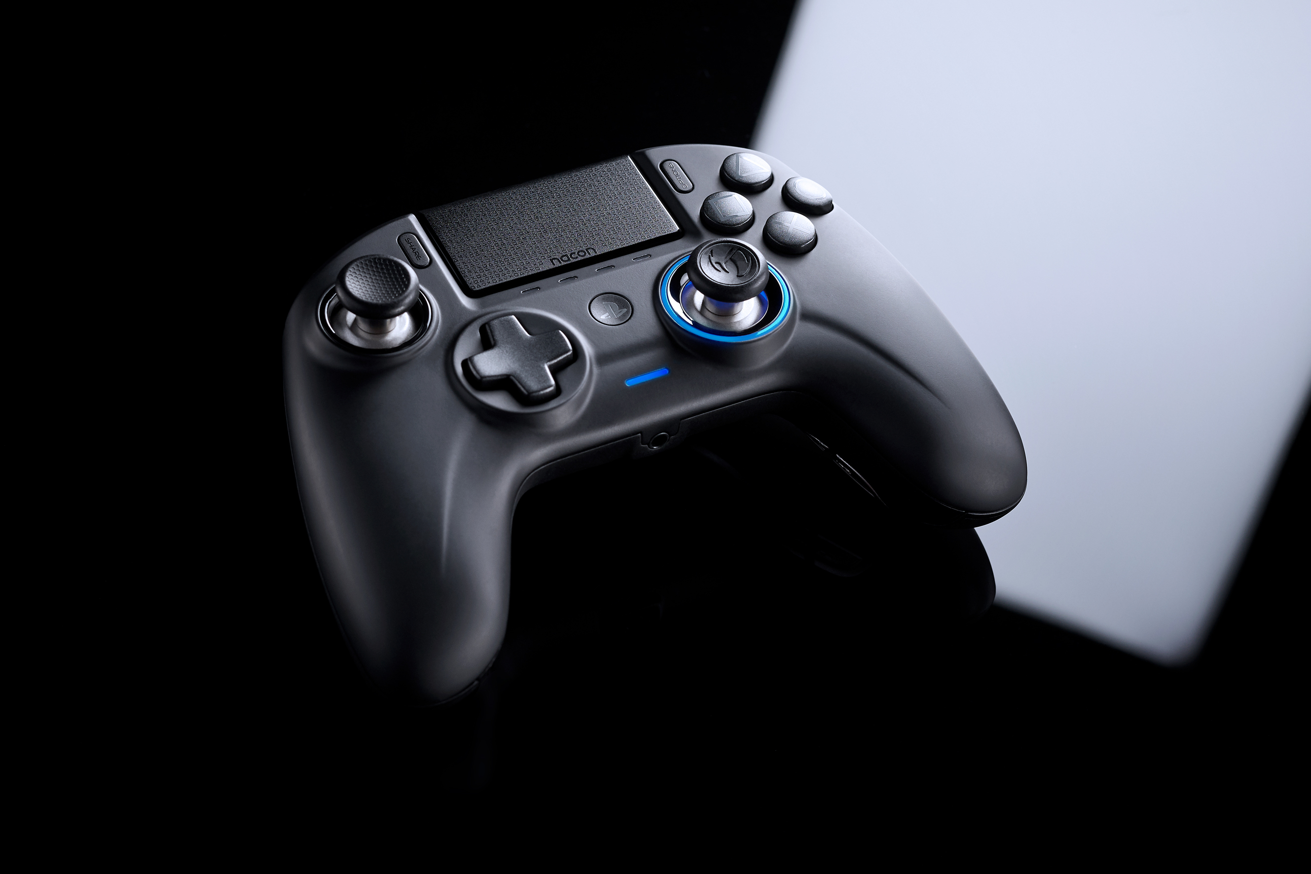 Mando de juego negro con botones y joysticks. Superficie negra reflectante. Luz azul.