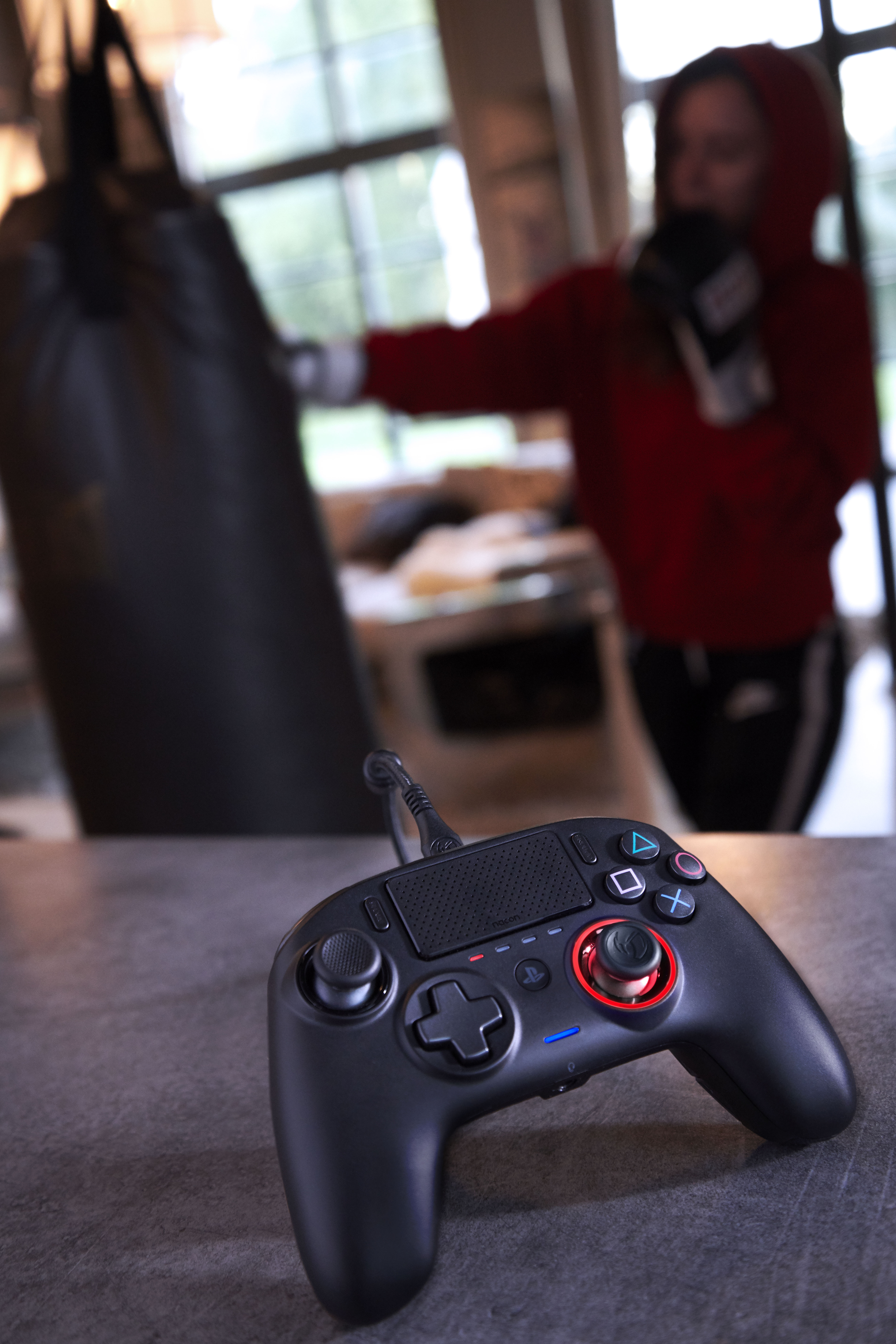 Czarny kontroler gier na stole, osoba boksująca w tle.