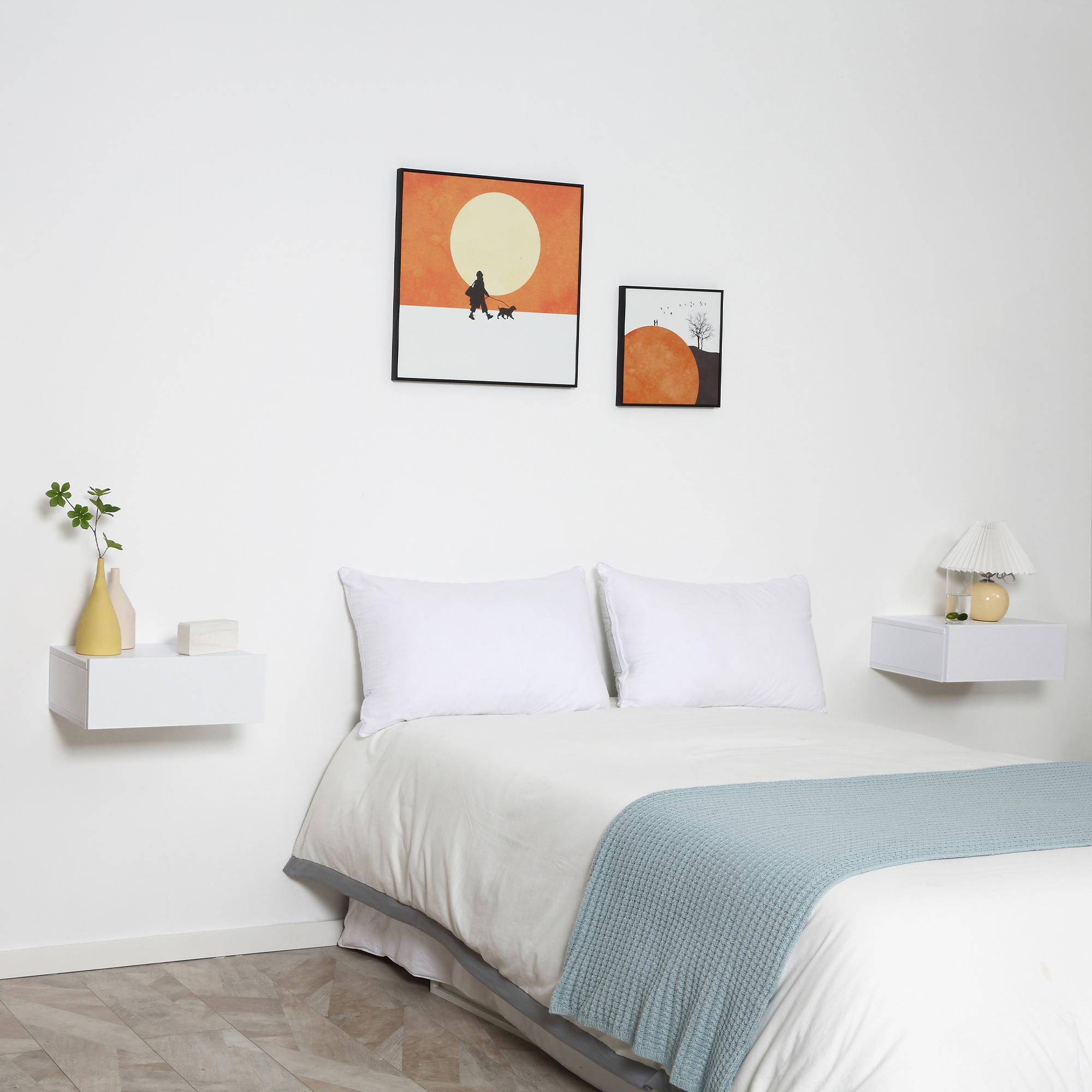 Una cama con almohadas blancas, manta azul, mesitas de noche y arte de pared.