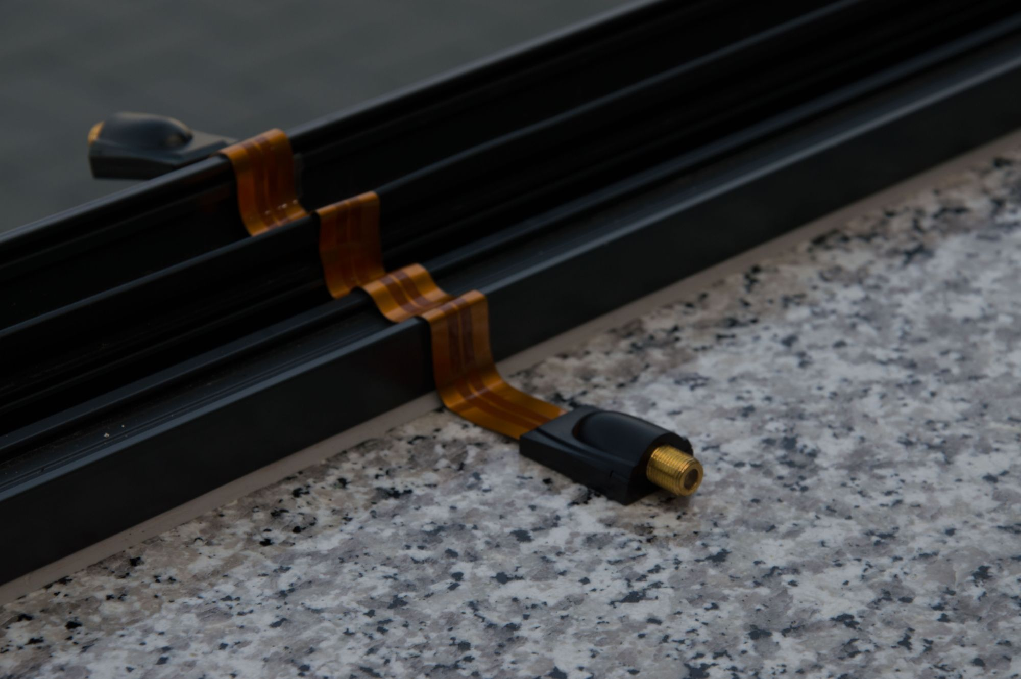 Schwarzes Kabel mit orangefarbenen Bändern, auf einer grauen Oberfläche platziert. Der Hintergrund ist unscharf.