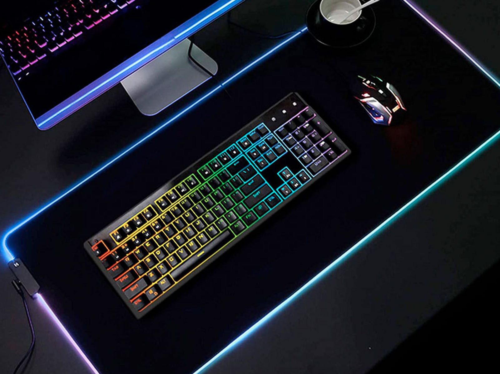 Un teclado y un ratón retroiluminados en un escritorio con una gran alfombrilla de ratón para juegos. El escritorio es oscuro.