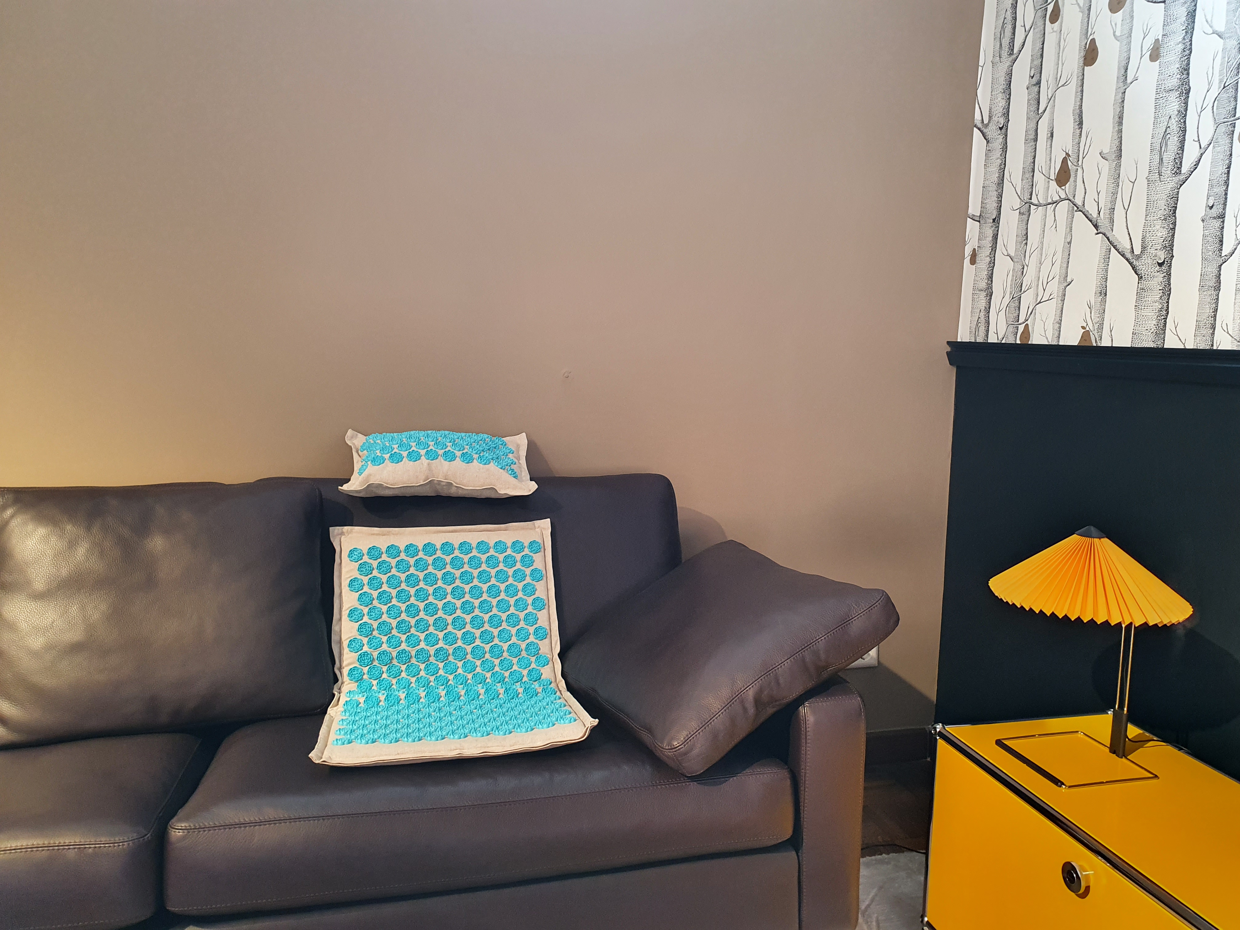 Braunes Ledersofa mit zwei Kissen und einem gelben Beistelltisch mit Lampe.