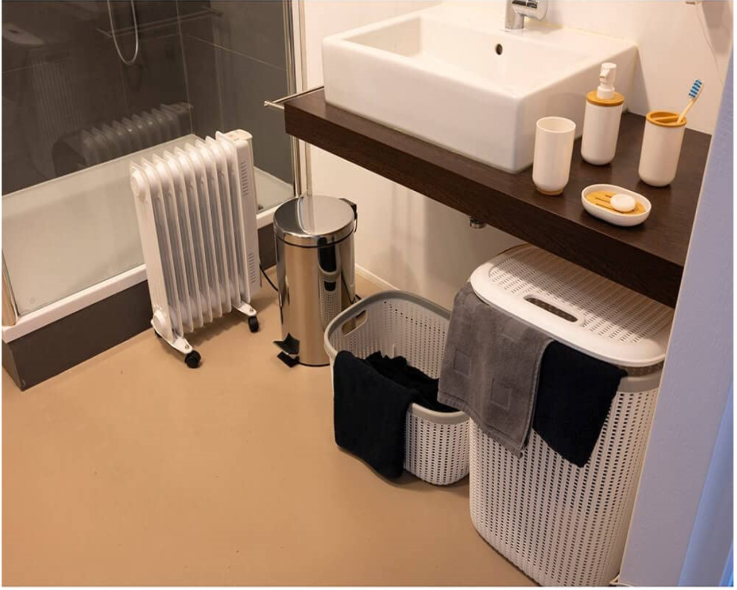 Badezimmer: weißes Waschbecken, Holzregal, Wäschekörbe, Heizkörper und Mülleimer auf dem Boden.