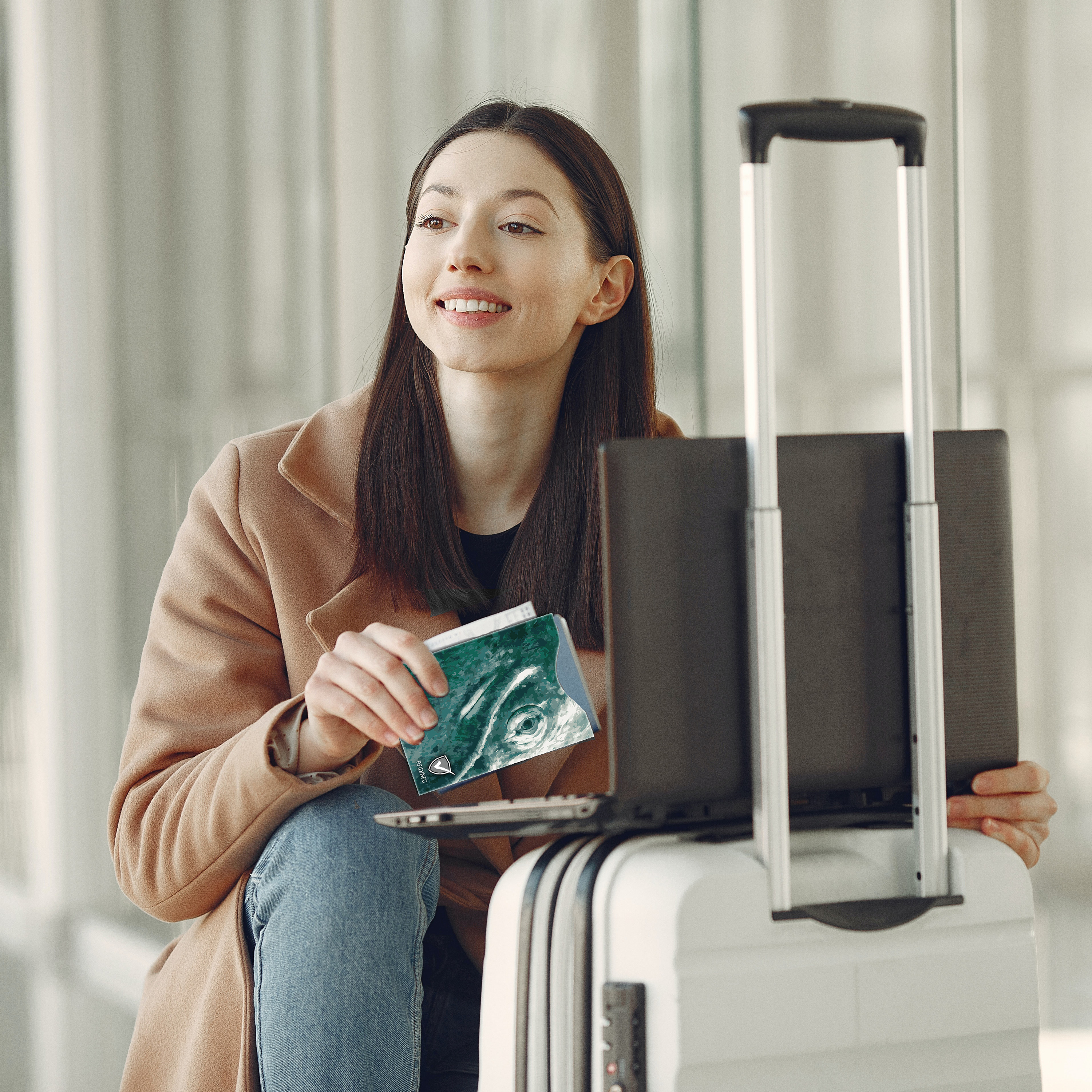 Eine Frau hält einen Reisepass und einen Laptop, Koffer davor. Lächelnd. Sonniger Hintergrund.