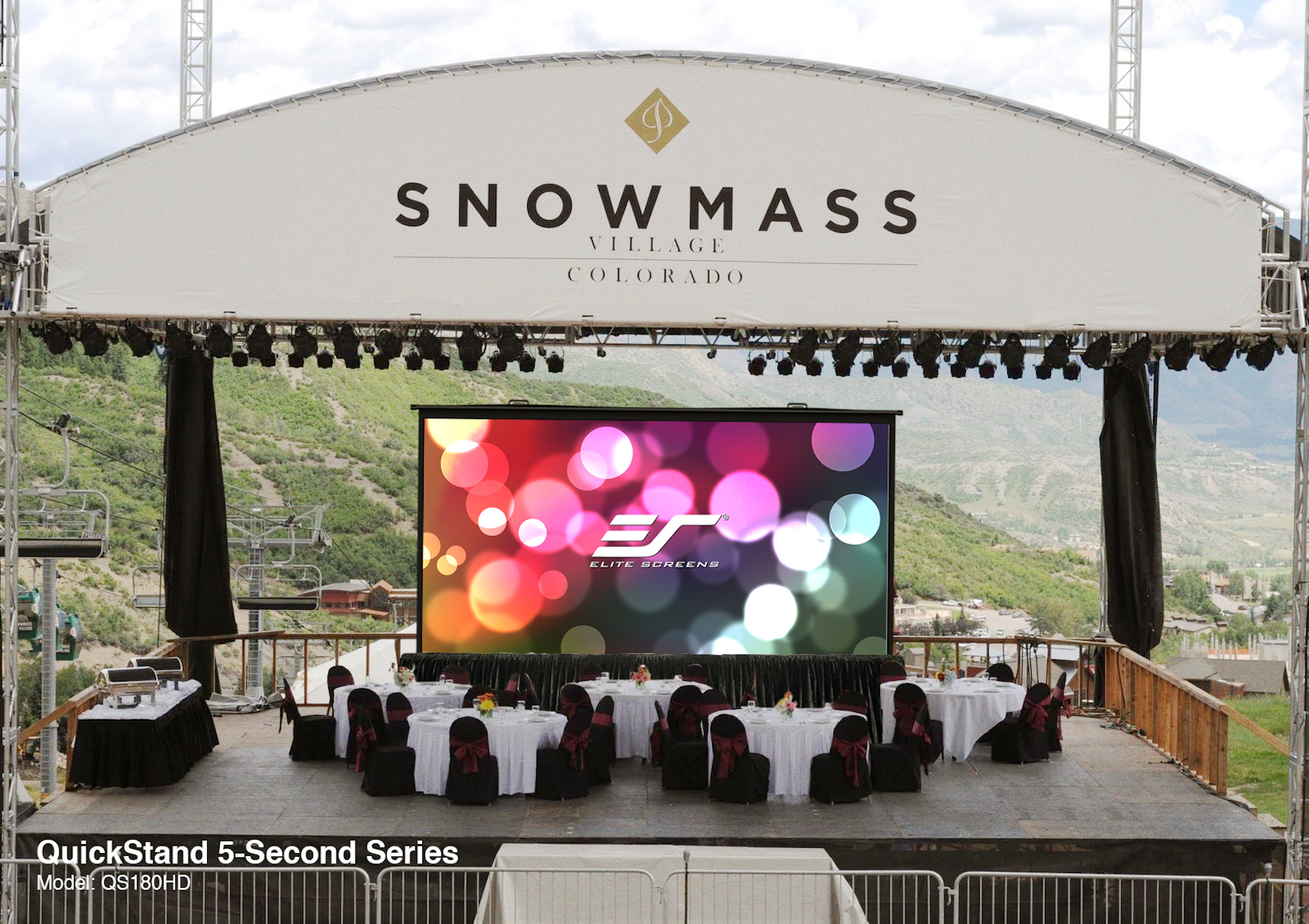 Outdoor-Bühne mit Bildschirm, der Bokeh-Lichter zeigt. Snowmass Village Banner. Tische und Stühle davor.