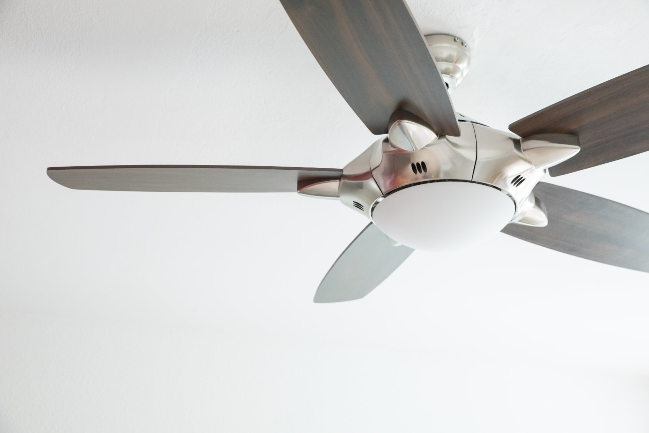 Ein Deckenventilator mit dunklen Holzblättern und einer weißen Leuchte.