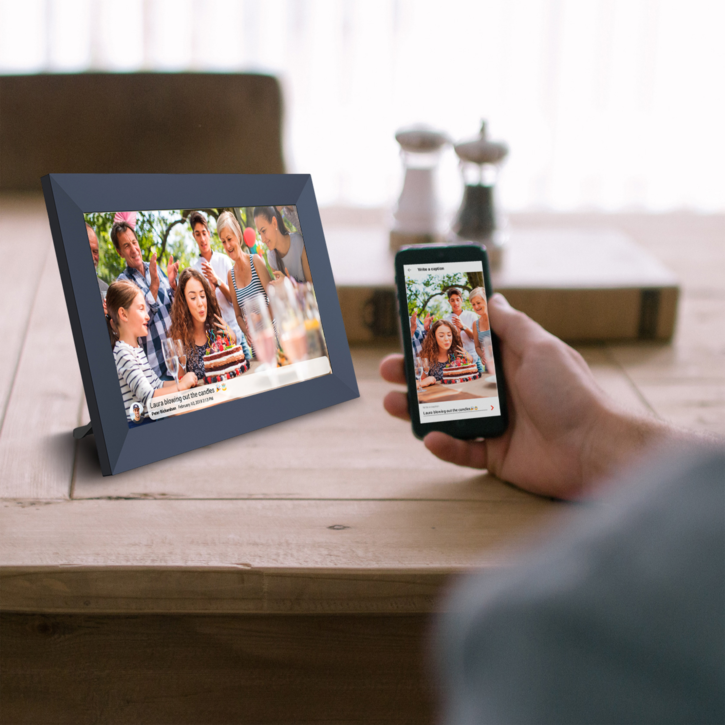 Osoba trzyma telefon obok cyfrowej ramki na zdjęcia pokazującej przyjęcie urodzinowe.