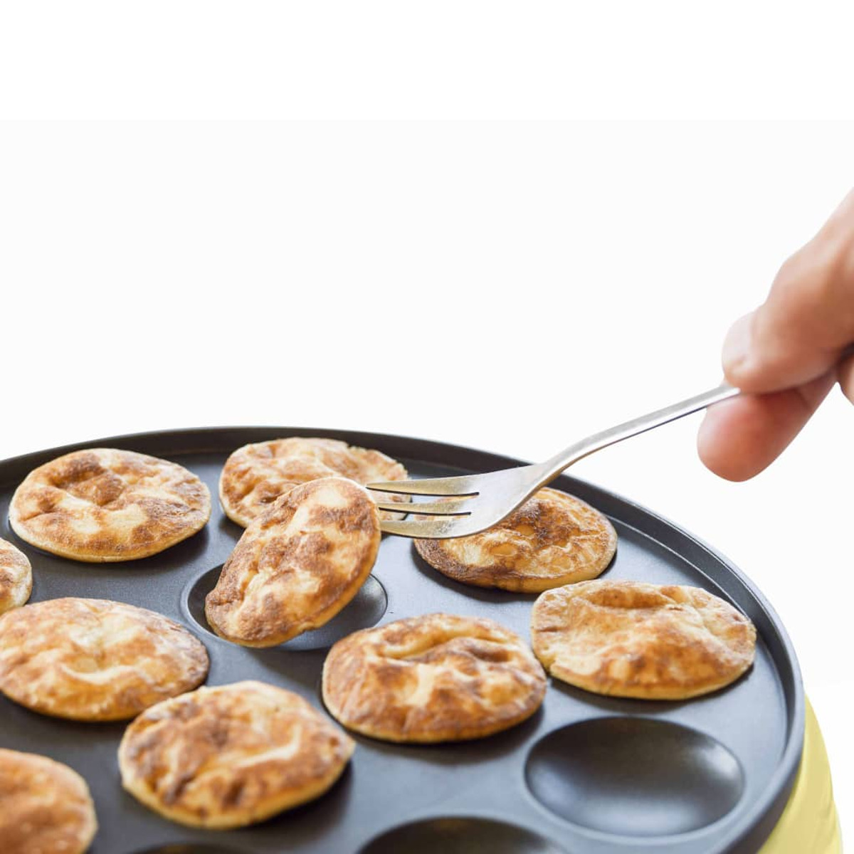 Ręka używająca widelca do wyjęcia naleśnika z małej patelni do naleśników.