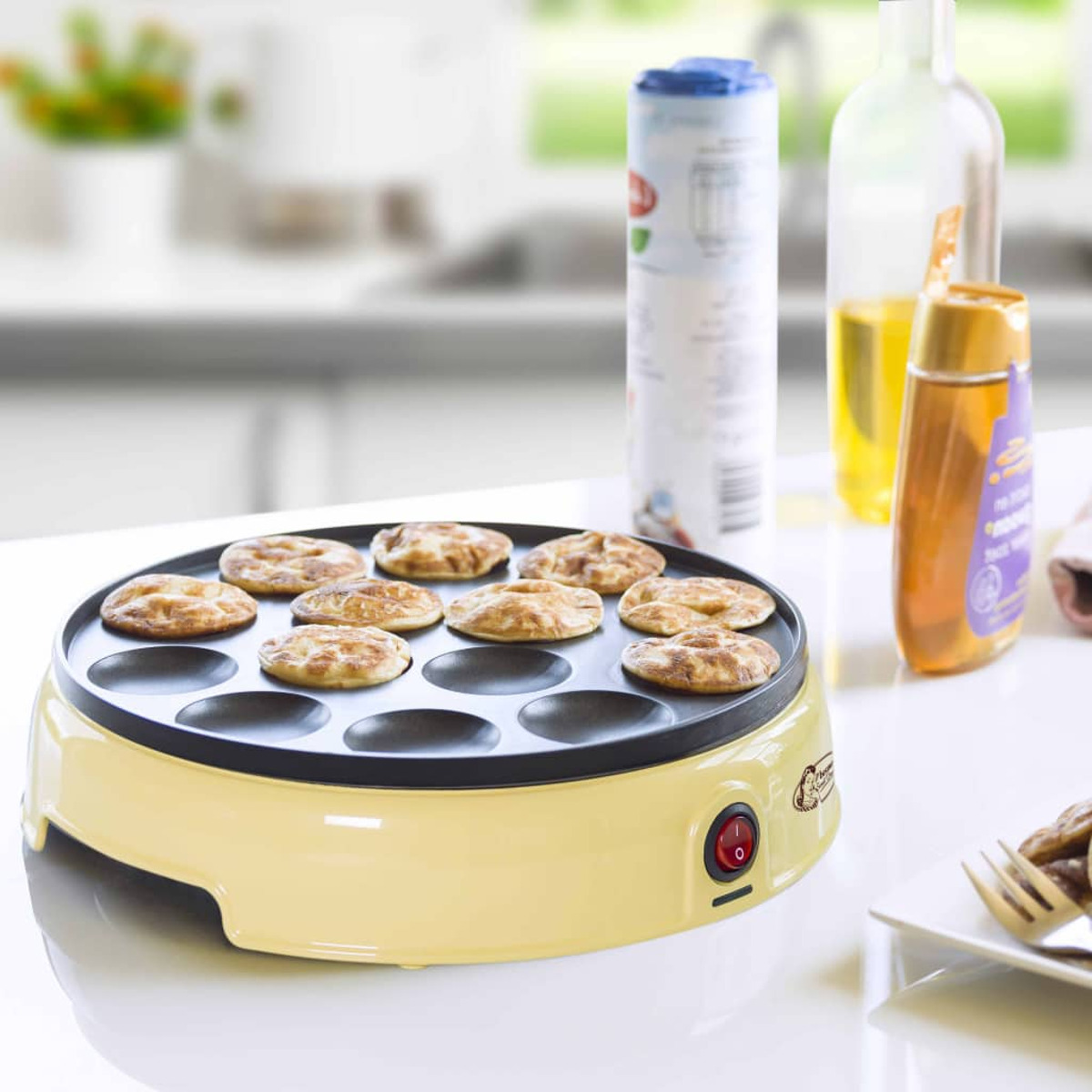 Żółta maszyna do naleśników z naleśnikami na wierzchu. Butelki miodu i oleju widoczne w tle.