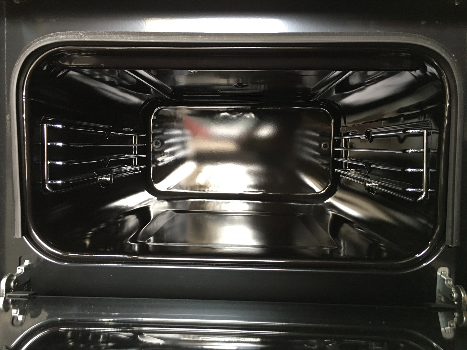 Interior de un horno. Es oscuro con rejillas y rieles metálicos para bandejas deslizantes.