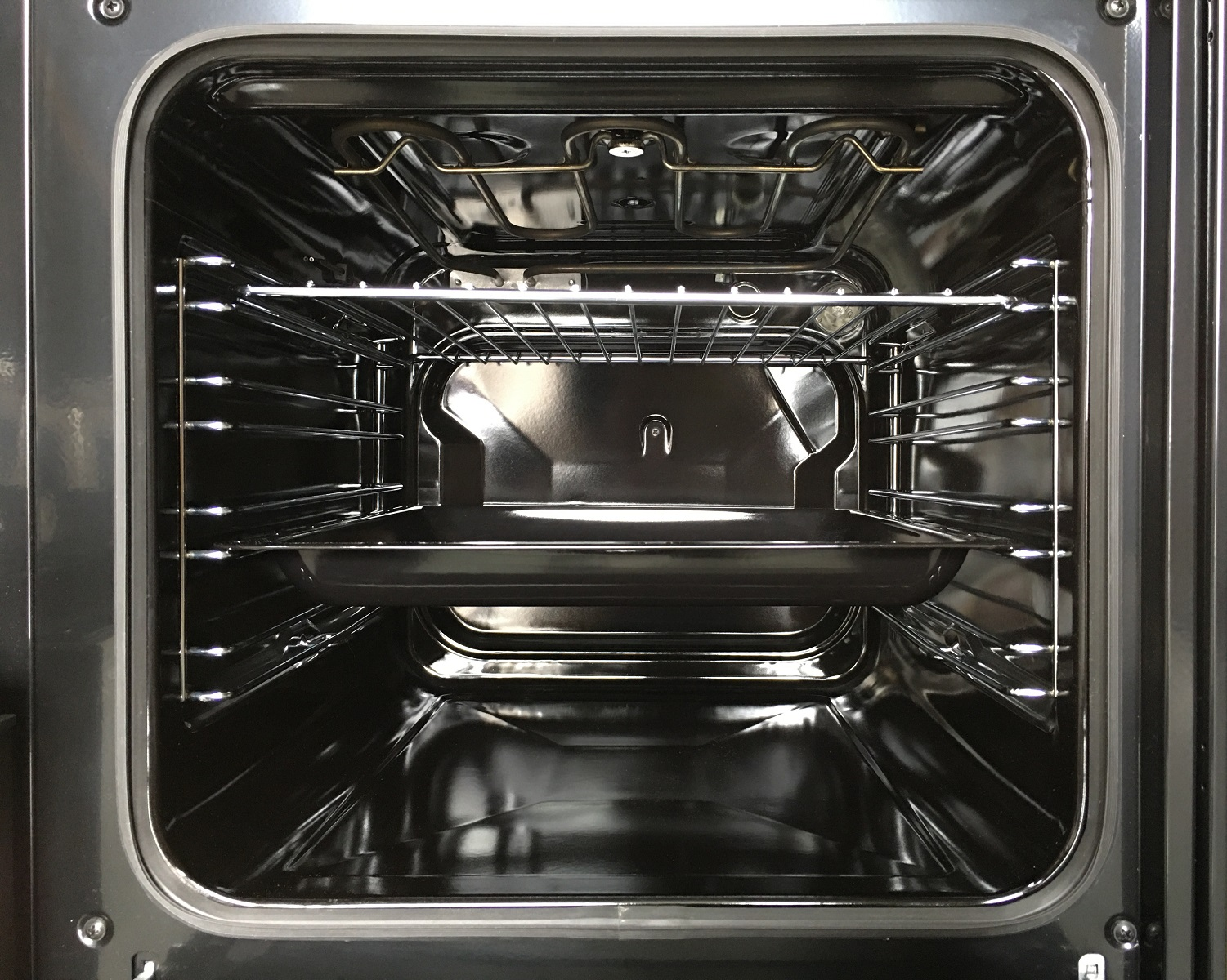 Interior de horno vacío con rejillas metálicas y superficie oscura y reflectante.