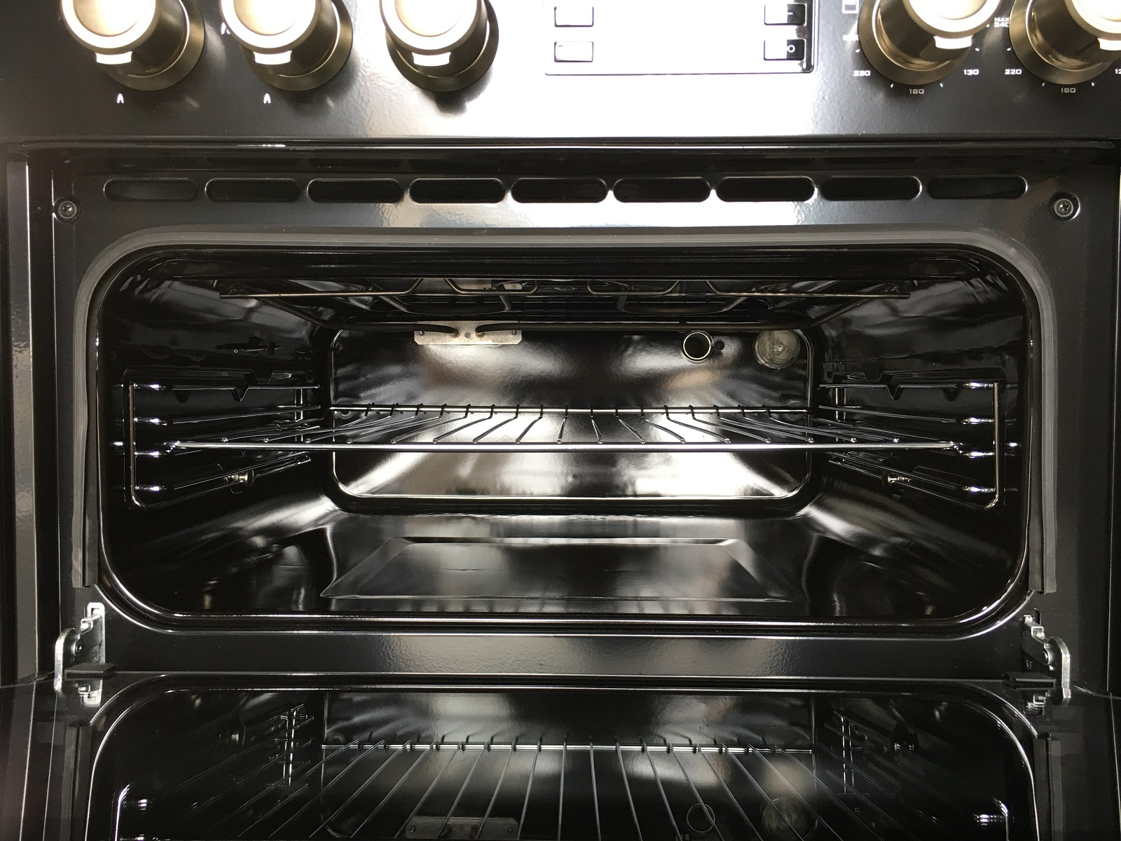 Interior de horno abierto. Interior negro con rejillas y luz. Los controles superiores son visibles.