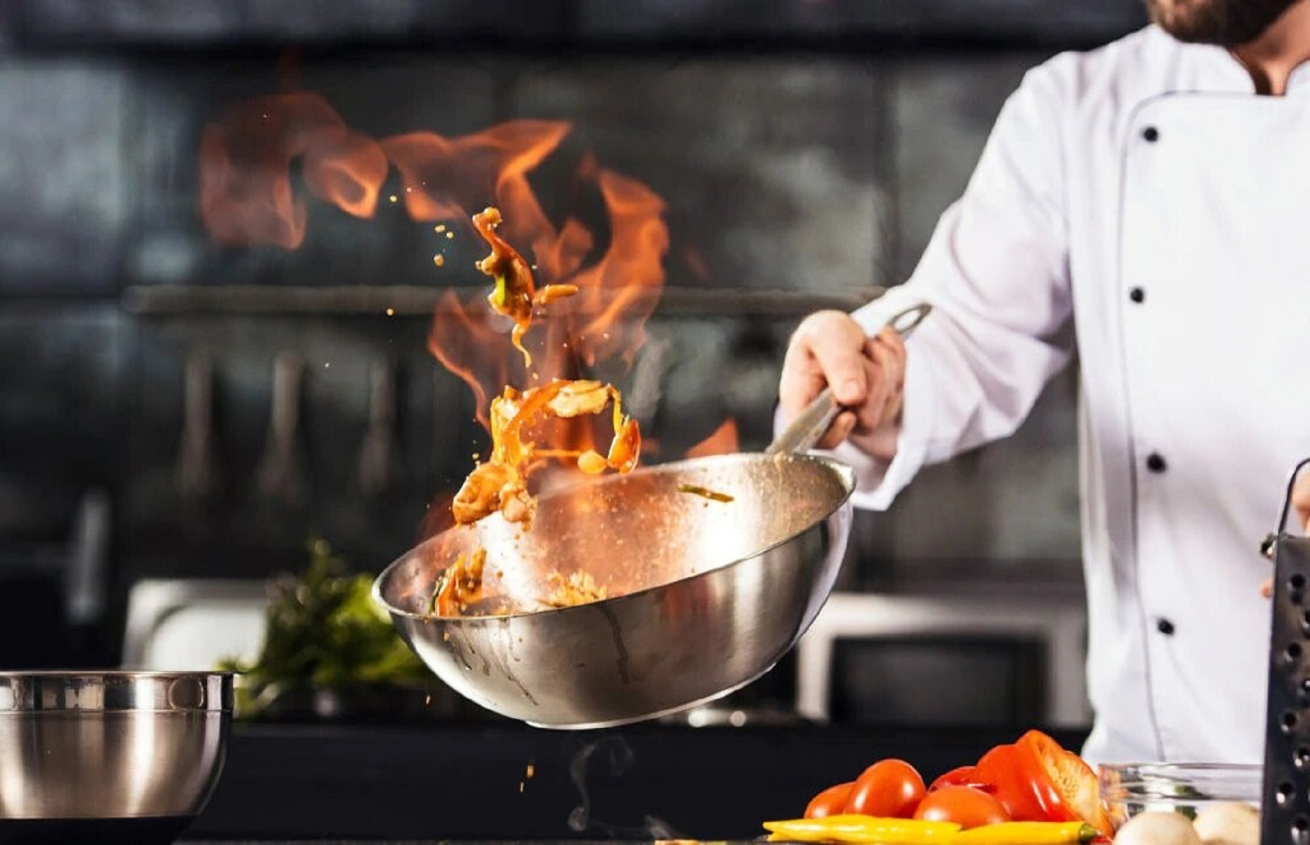Un chef lanzando comida en una sartén con llamas, en un ambiente de cocina.