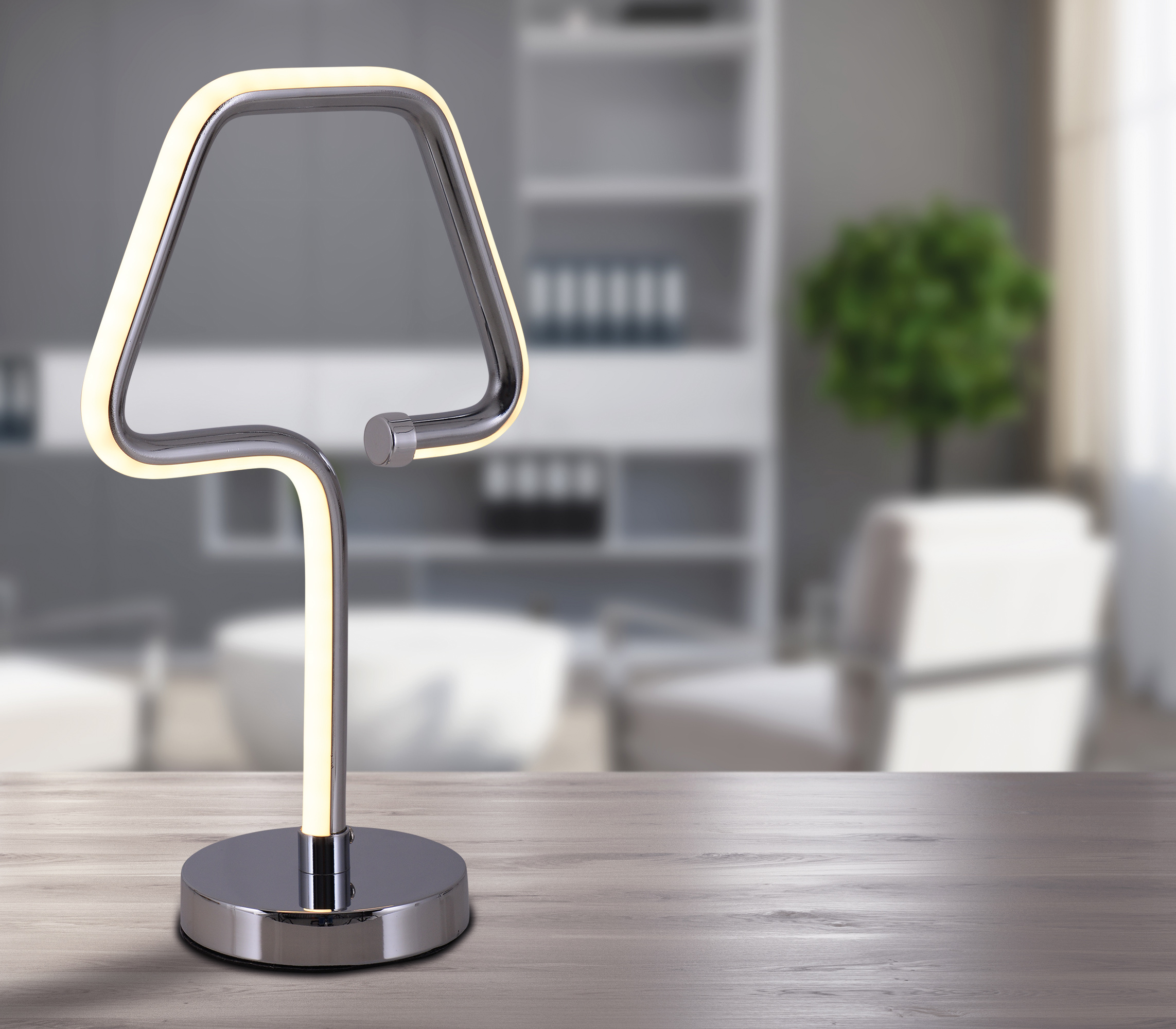 Moderne Chromlampe mit dreieckiger Oberseite, auf Holztisch, unscharfer Hintergrund.